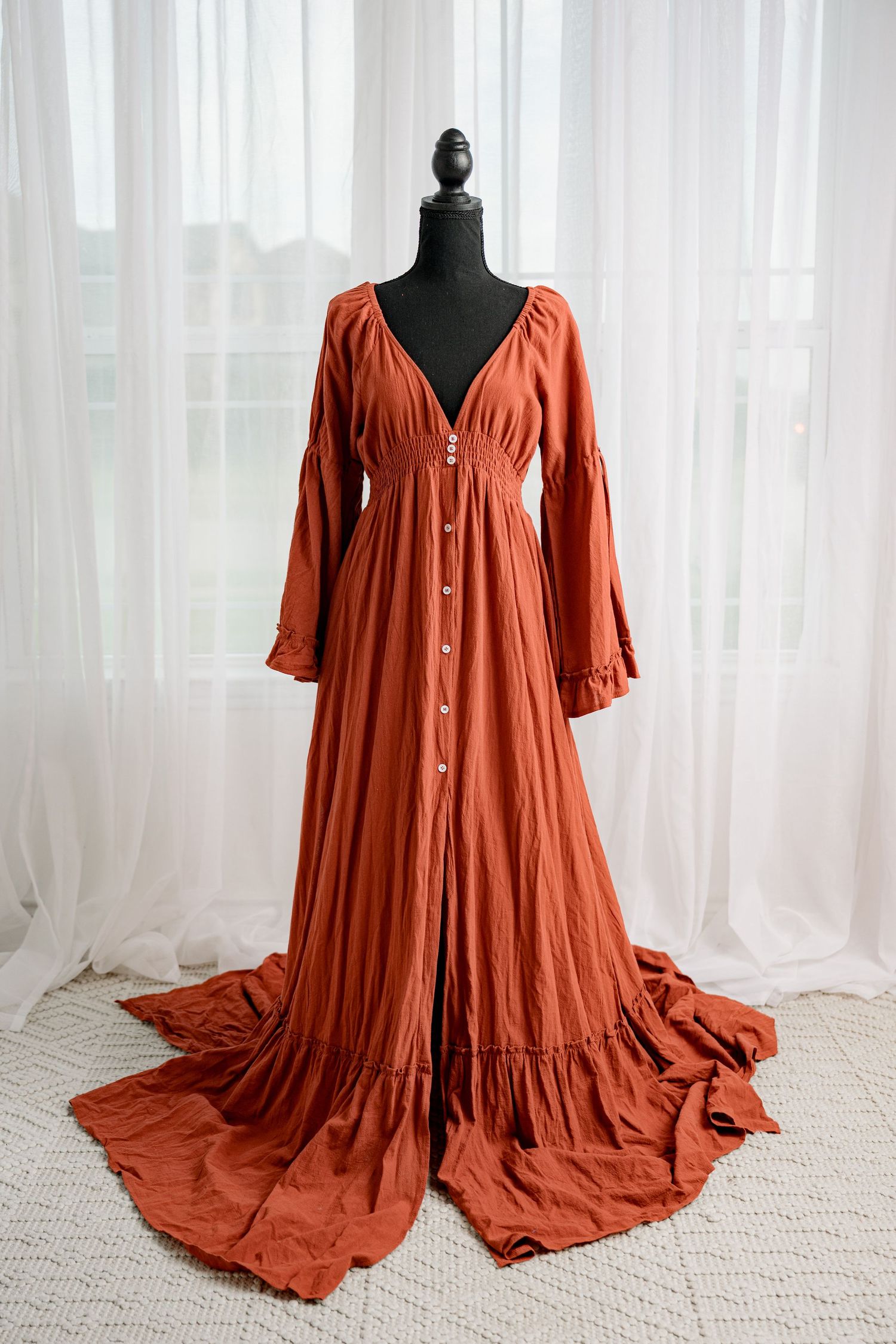 Rust orange long sleeve button-front maxi dress with ruffle hem on black mannequin.