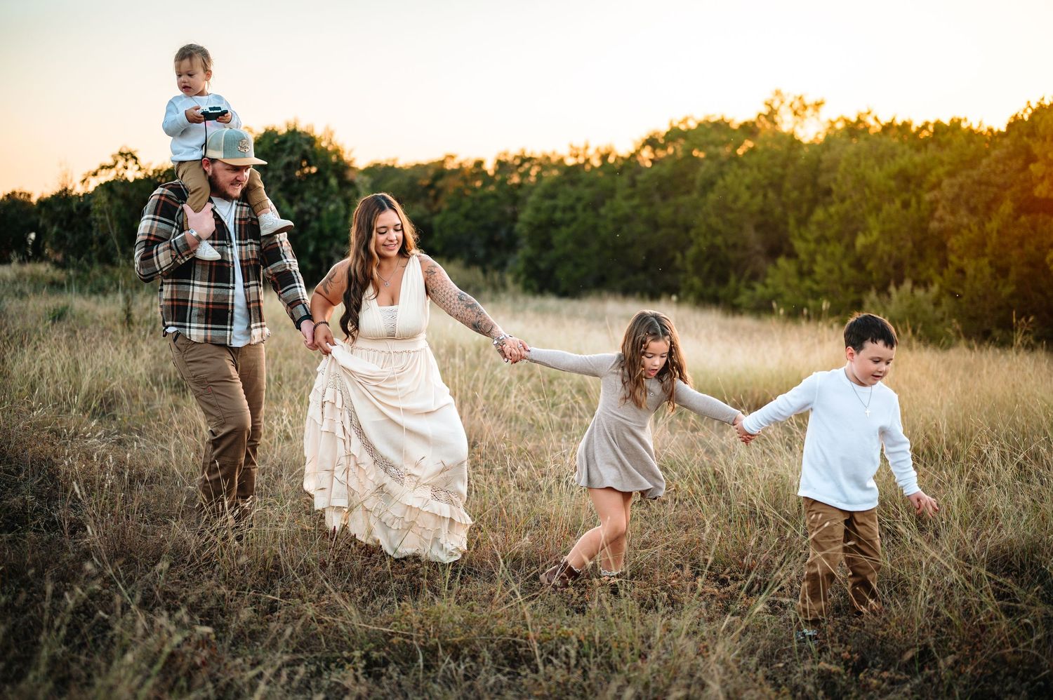 Family of five walking through golden field at sunset, mother wearing a lace boho maxi dress.