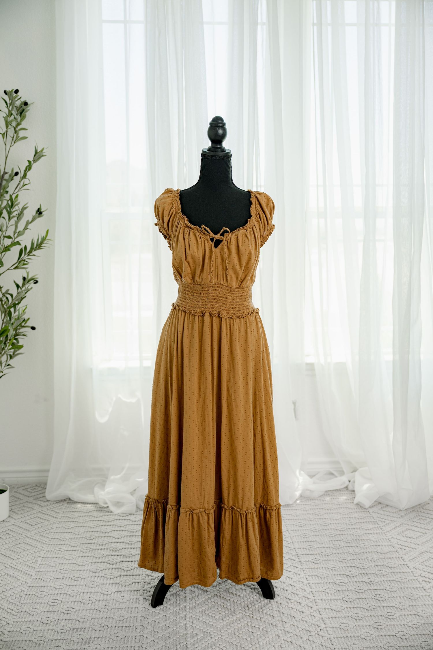Mustard yellow midi dress with puff sleeves, smocked bodice, and tiered ruffle hem on black mannequin.
