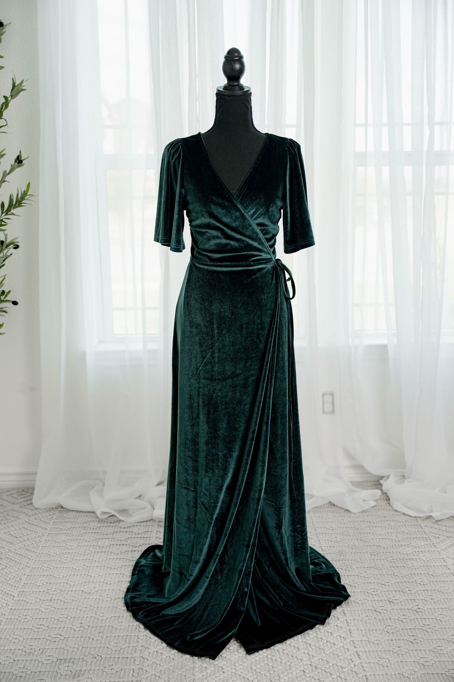 Emerald green velvet wrap maxi dress with short sleeves and side tie on a black mannequin.