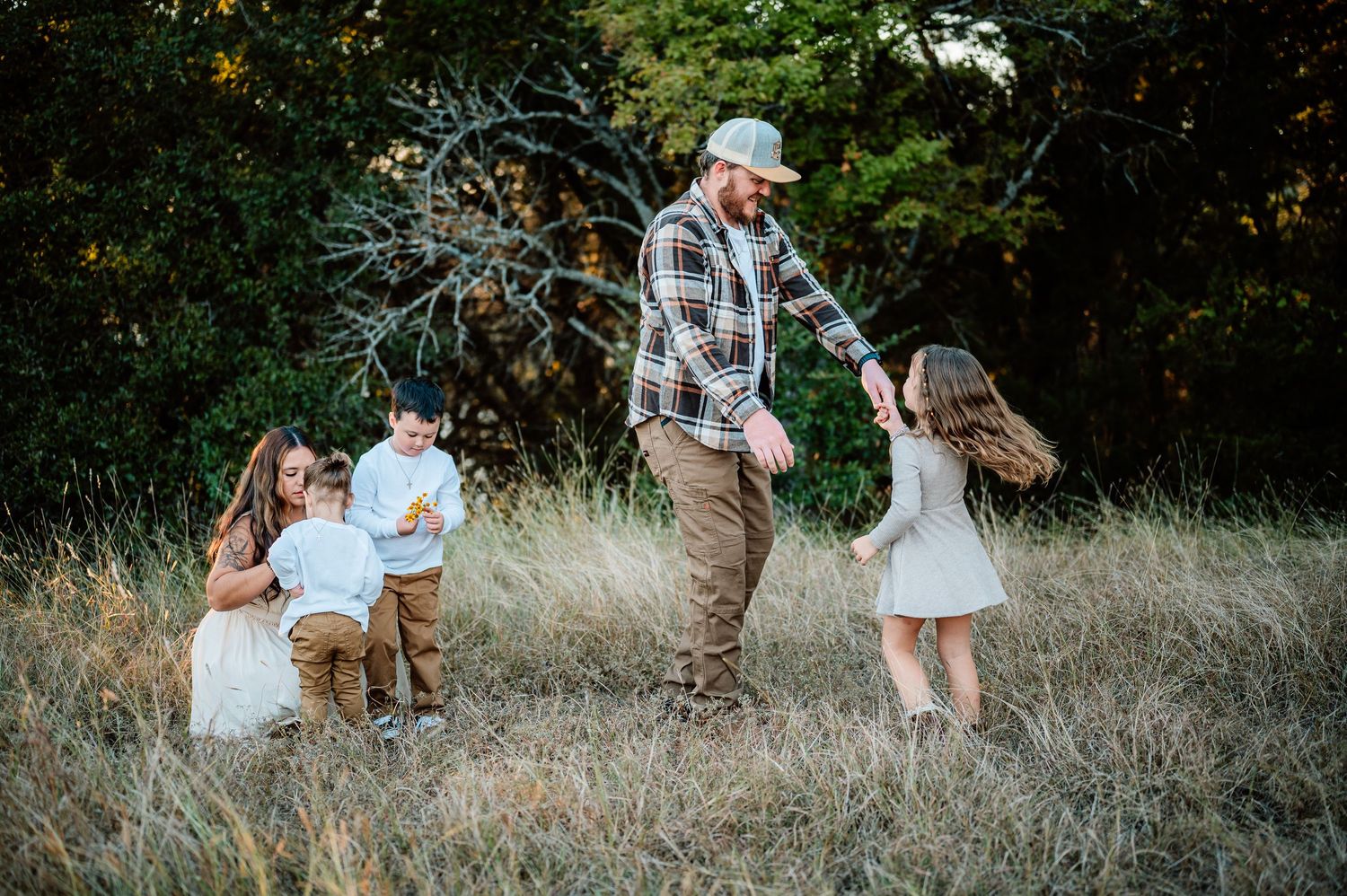 Father playing with his three children in a golden meadow surrounded by autumn trees.