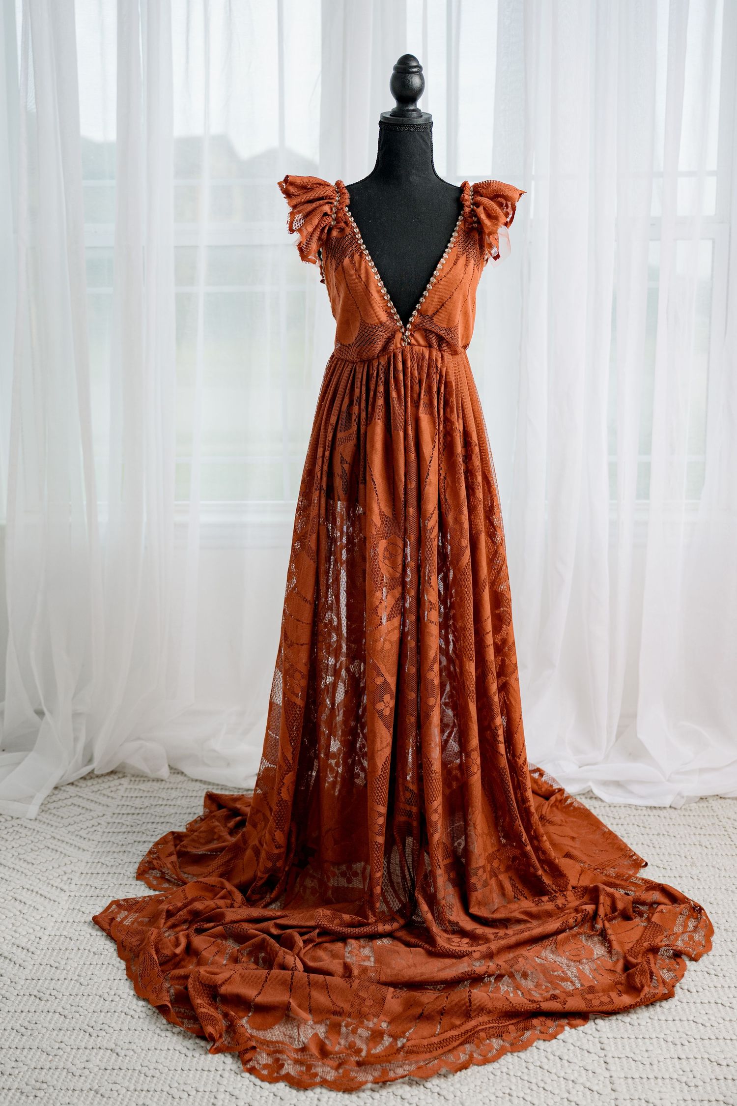 Rust orange lace gown with ruffle cap sleeves and deep V-neckline on black mannequin.