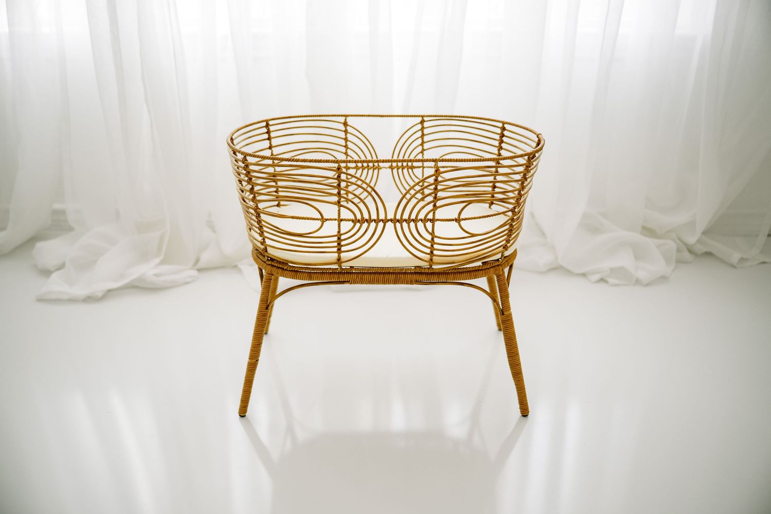 Gold rattan oval bassinet with decorative wire design on legs.