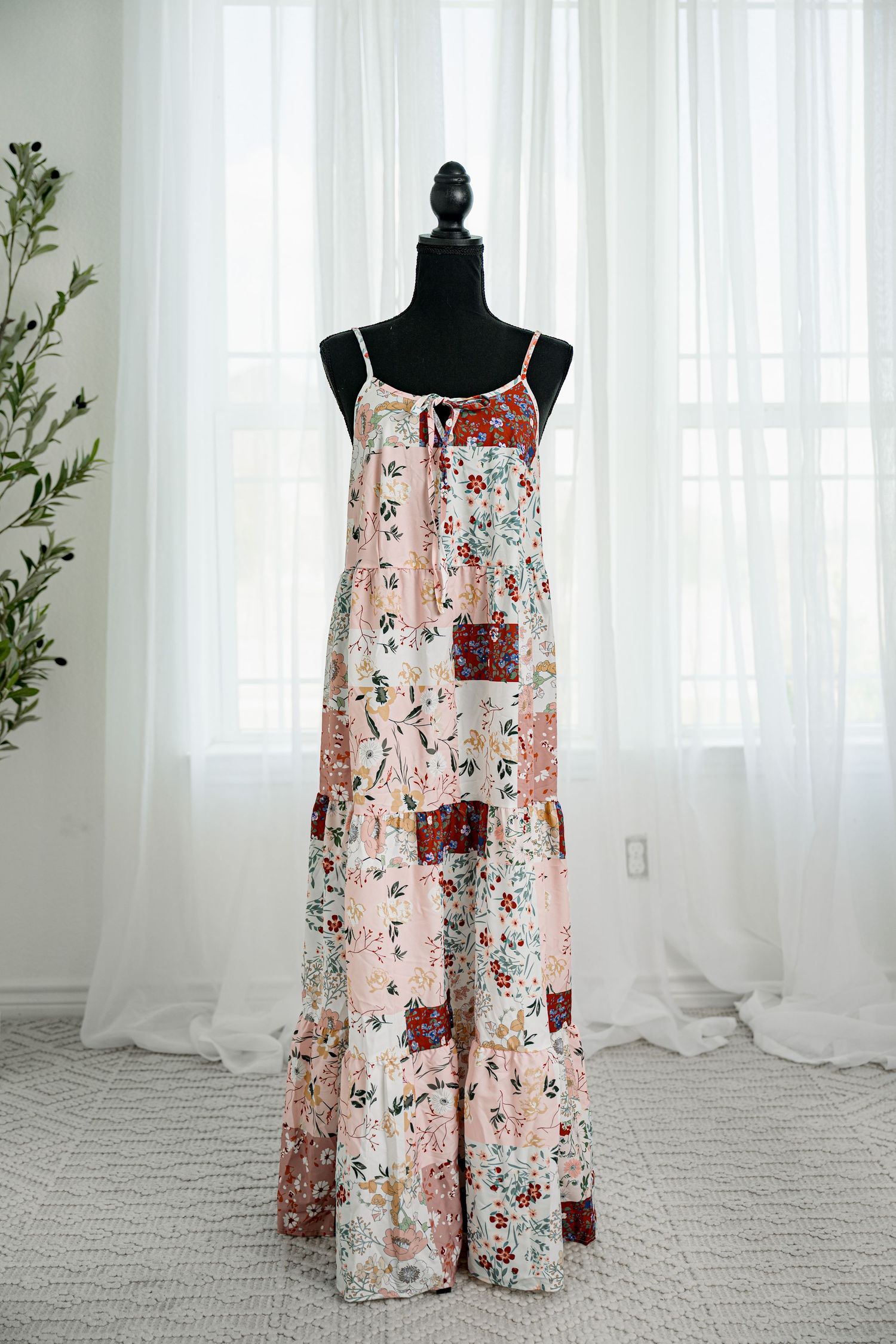 Pink patchwork floral spaghetti strap tiered maxi dress with front tie detail on black mannequin.
