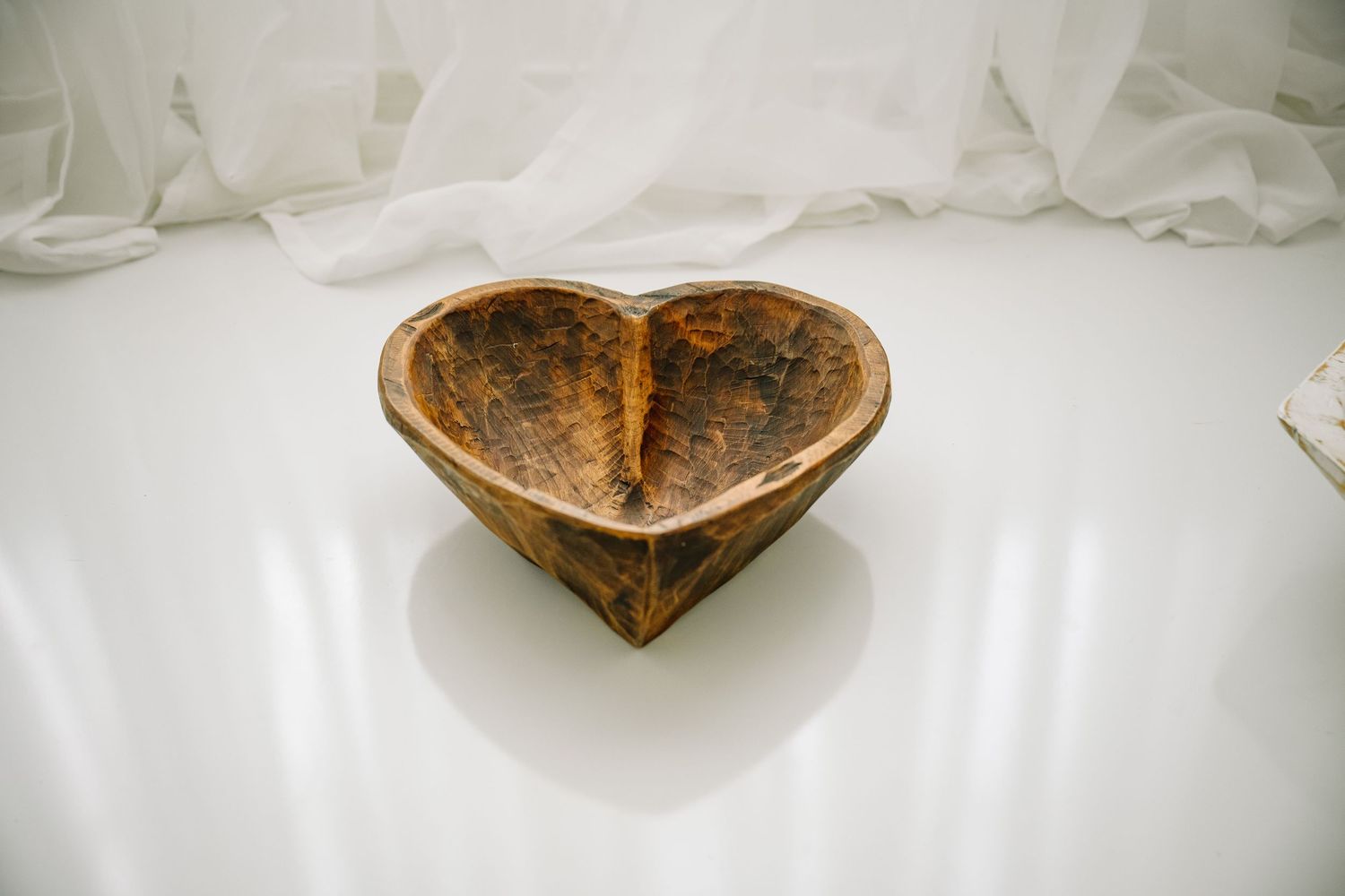 Heart-shaped dark burl wood bowl on a white reflective surface.