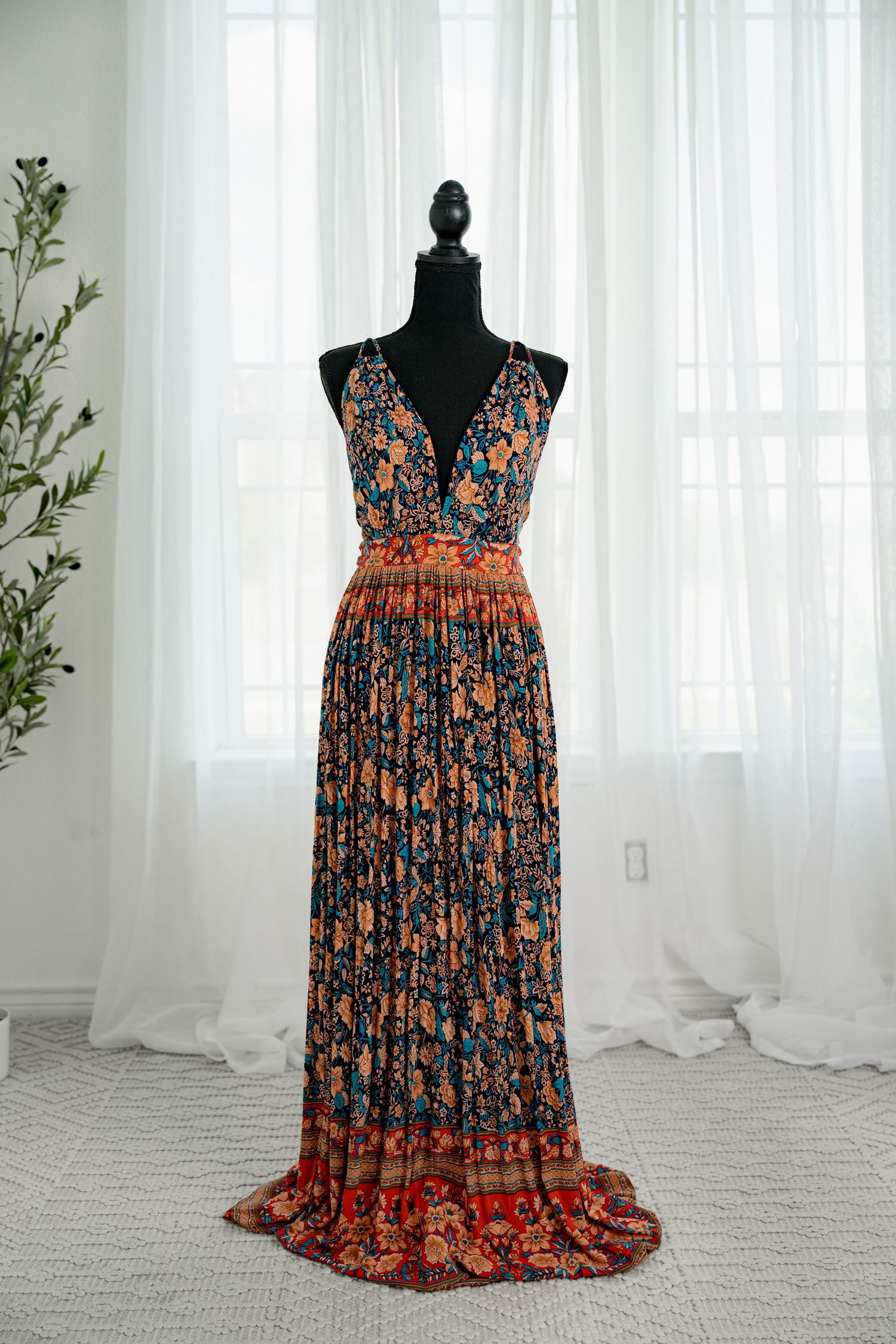 Dark floral boho maxi dress with deep V-neck, pleated skirt, and vibrant orange and teal print on mannequin.