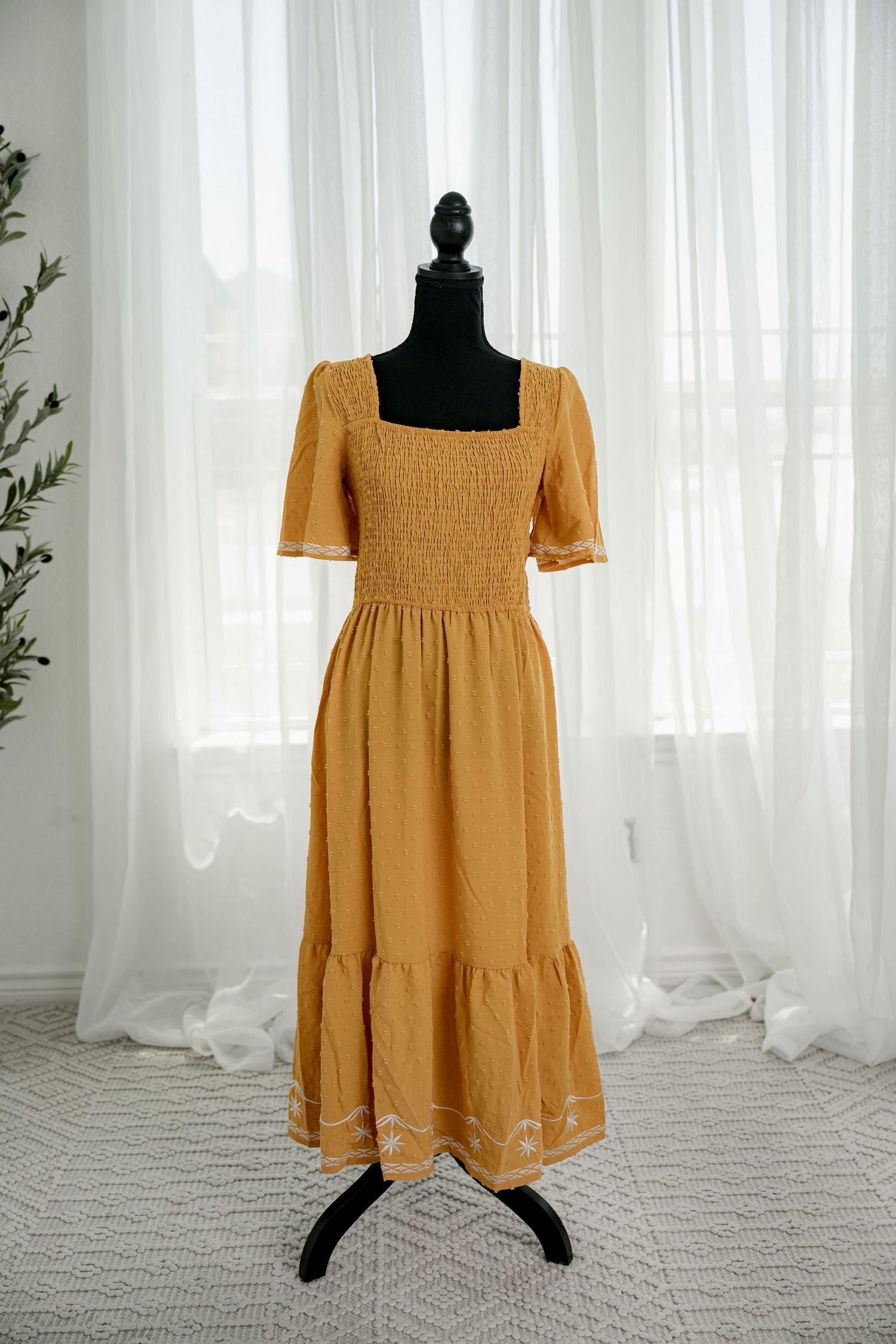 Golden yellow midi dress with square neck, smocked bodice, short sleeves, and embroidered hem on mannequin.