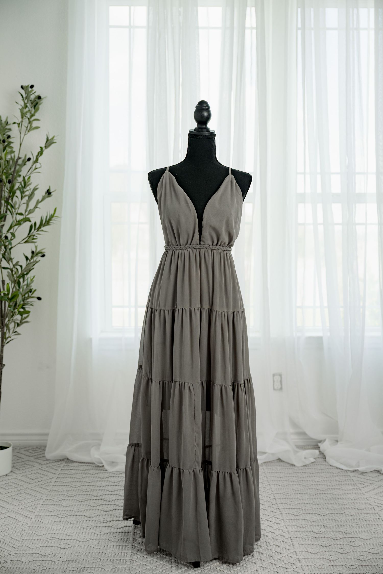 Olive gray spaghetti strap deep V-neck tiered maxi dress on black mannequin against white curtains.