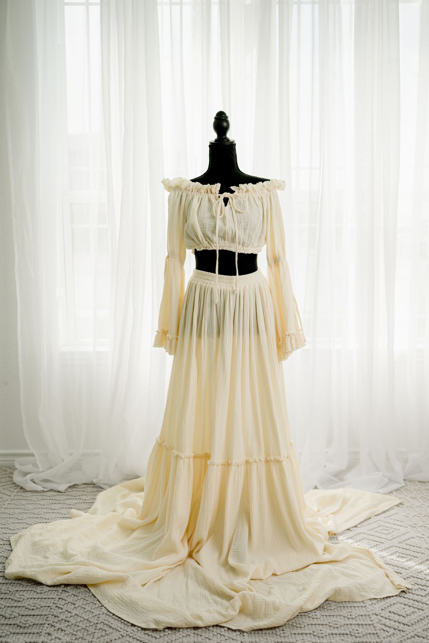Elegant cream off-shoulder two-piece bridal gown with long bell sleeves and flowing maxi skirt displayed on black mannequin.