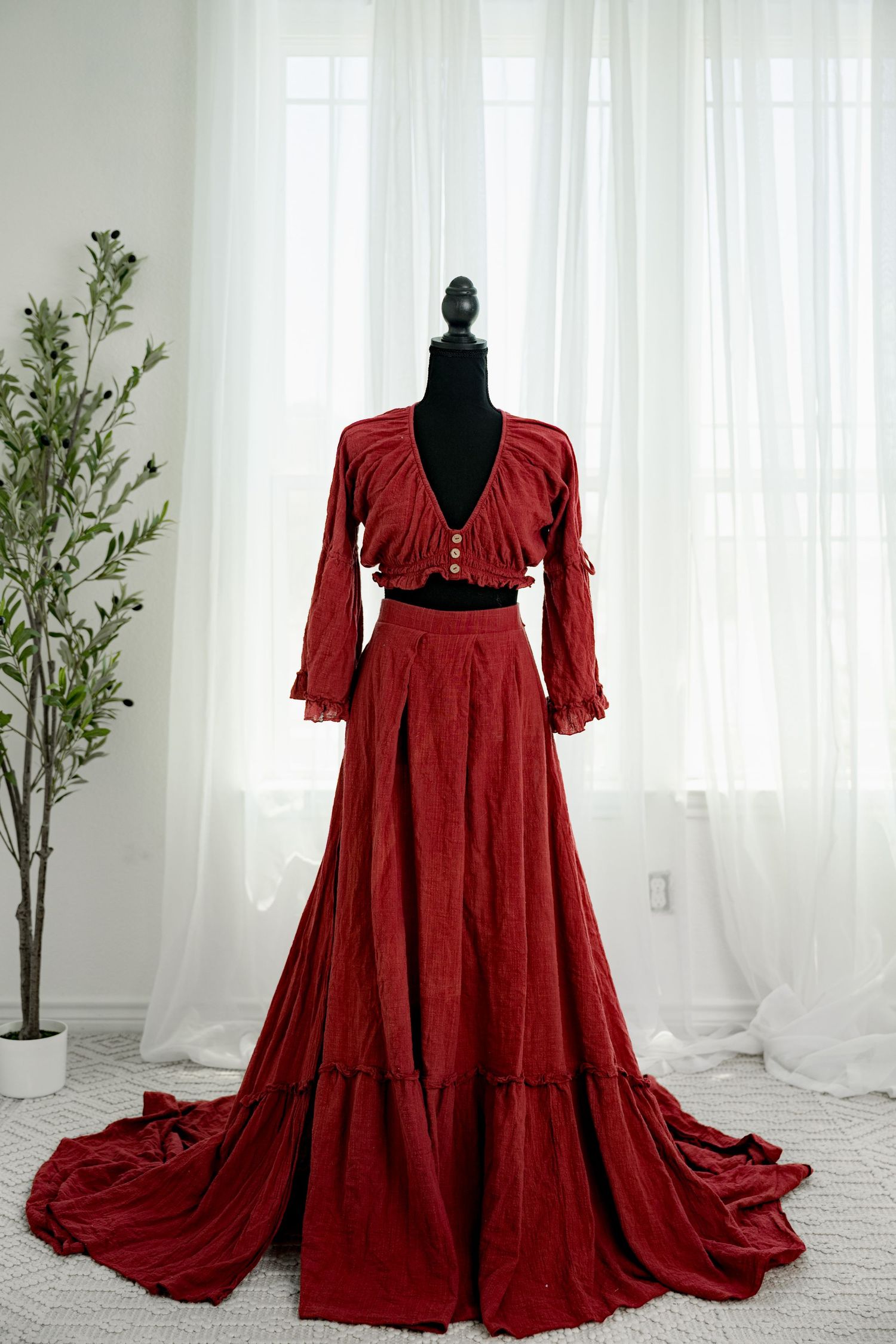 Deep red two-piece set with long ruffled sleeves crop top and pleated maxi skirt with train on mannequin.