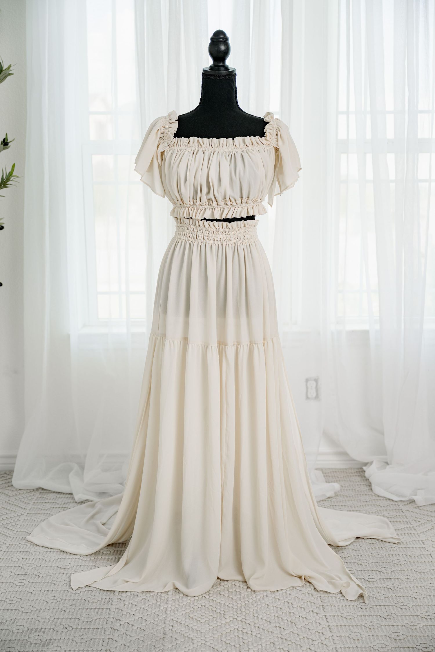 Cream off-shoulder smocked boho chiffon maxi dress with tiered skirt on a black mannequin.
