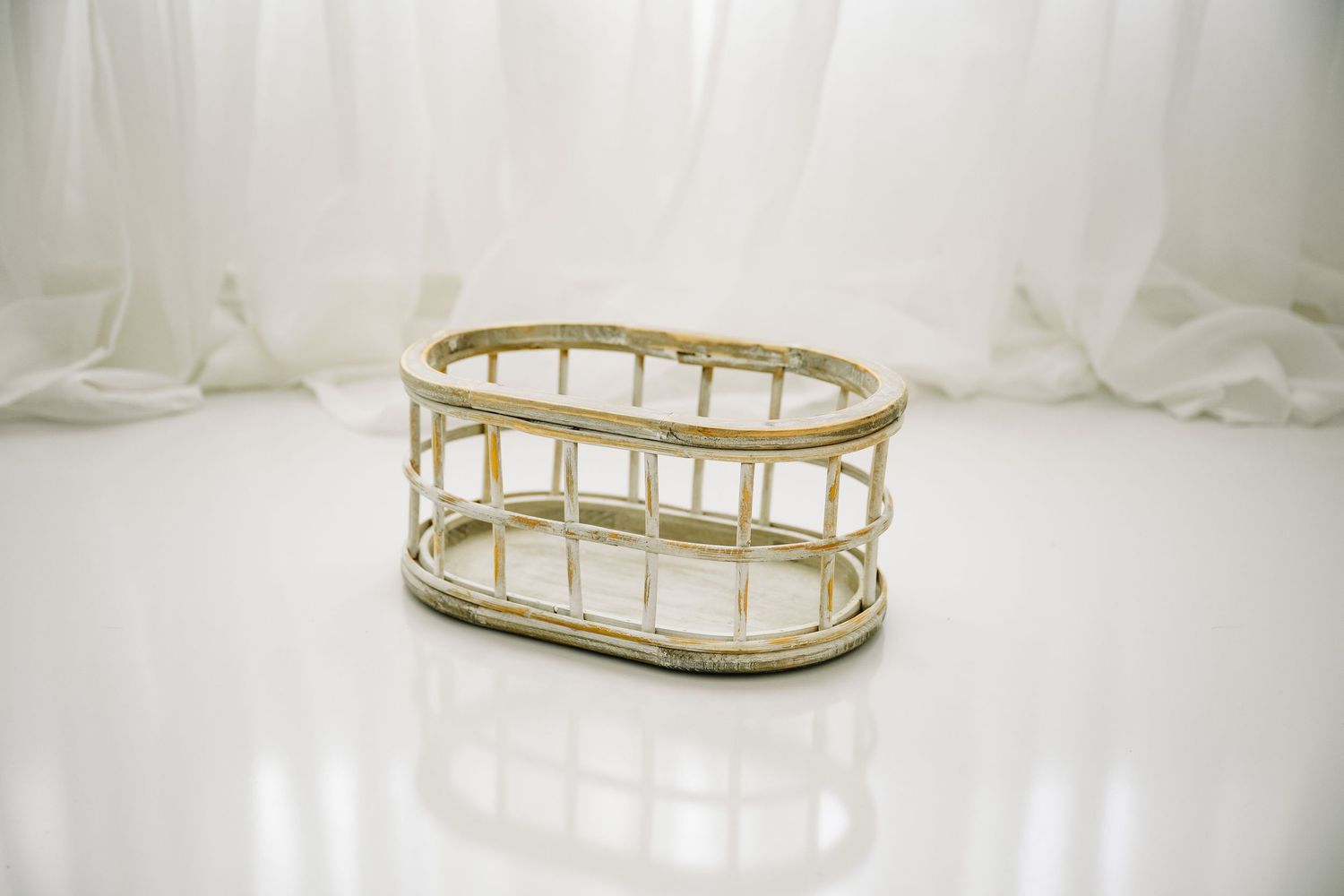 Oval wicker basket with gold trim on a white reflective surface.