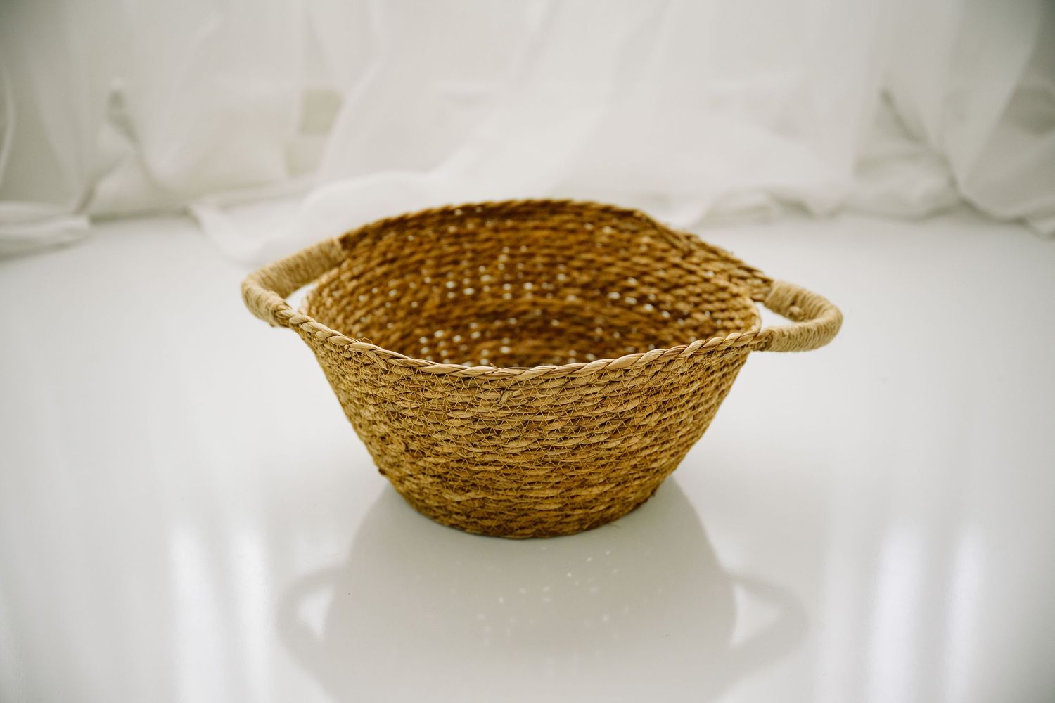 Natural woven seagrass basket with rope handles on white surface.
