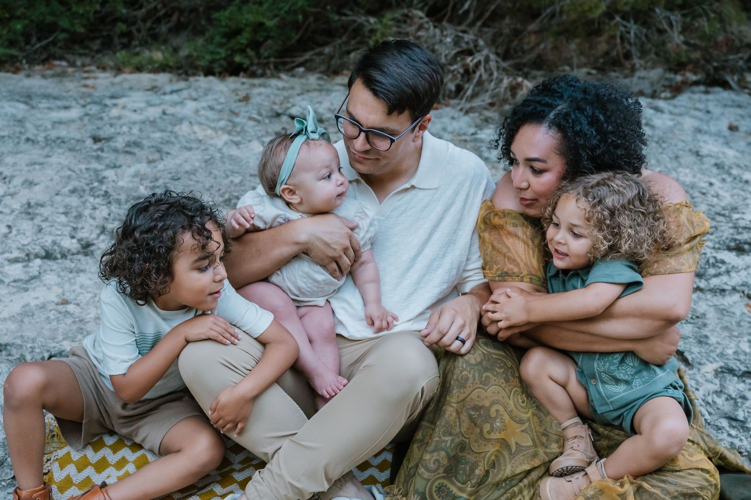 Family of five sitting together on a blanket at the beach, sharing a warm and loving moment.