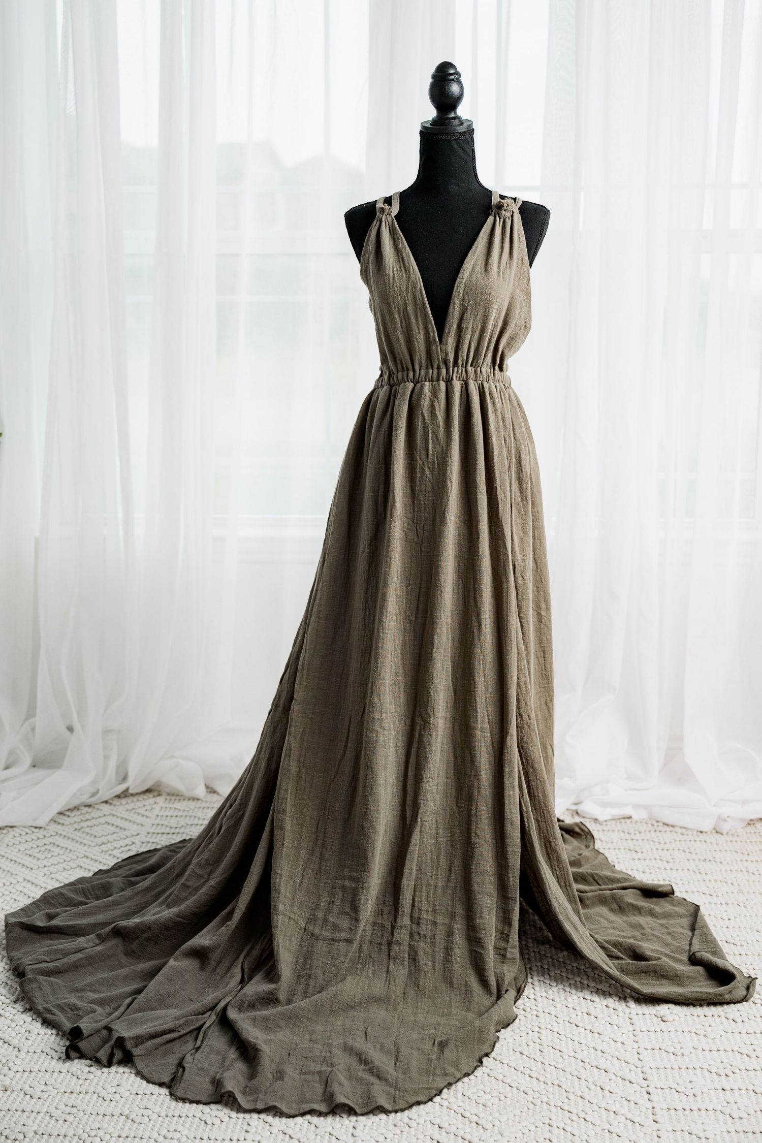 Elegant olive green linen maxi dress with deep V-neck and flowing train displayed on a black mannequin.