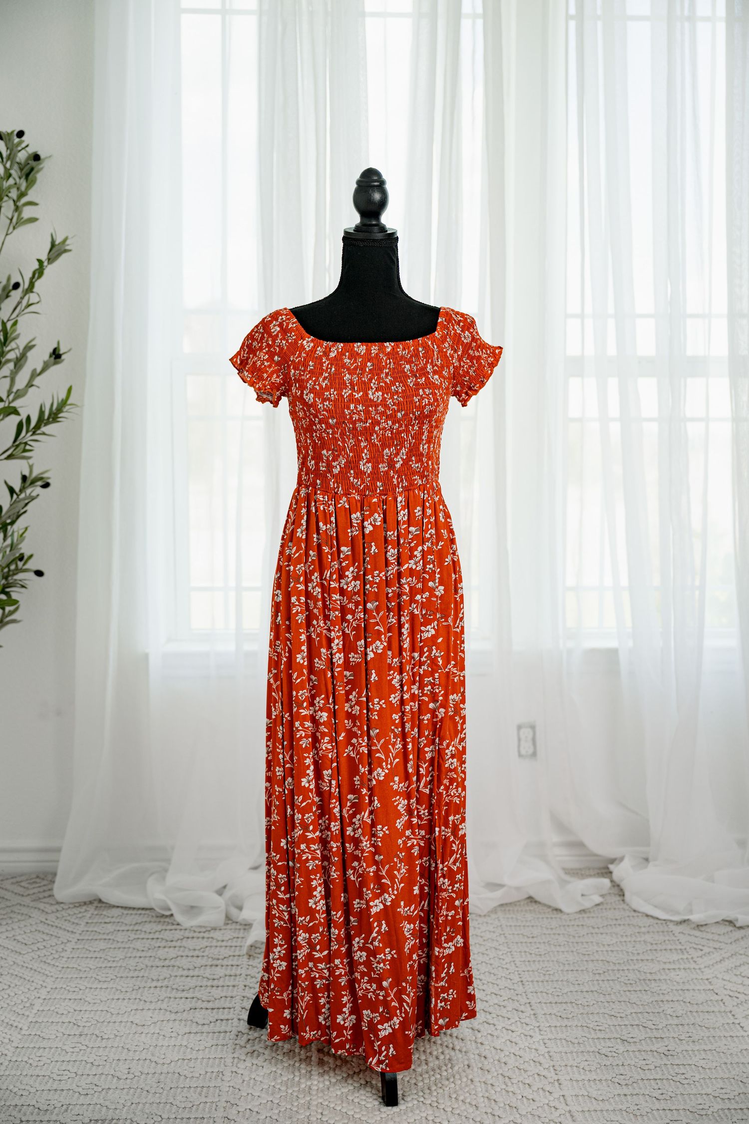 Red floral off-shoulder smocked bodice maxi dress displayed on a black mannequin.