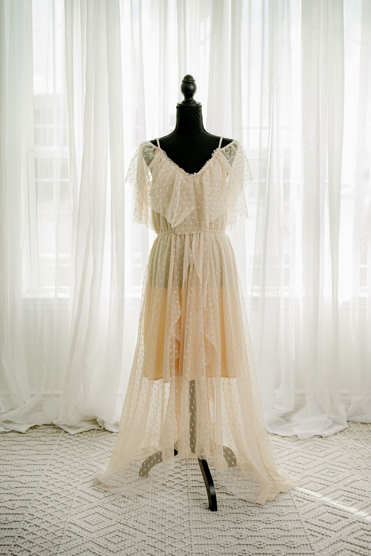Elegant ivory lace wedding dress with flutter sleeves displayed on a black mannequin against sheer white curtains.
