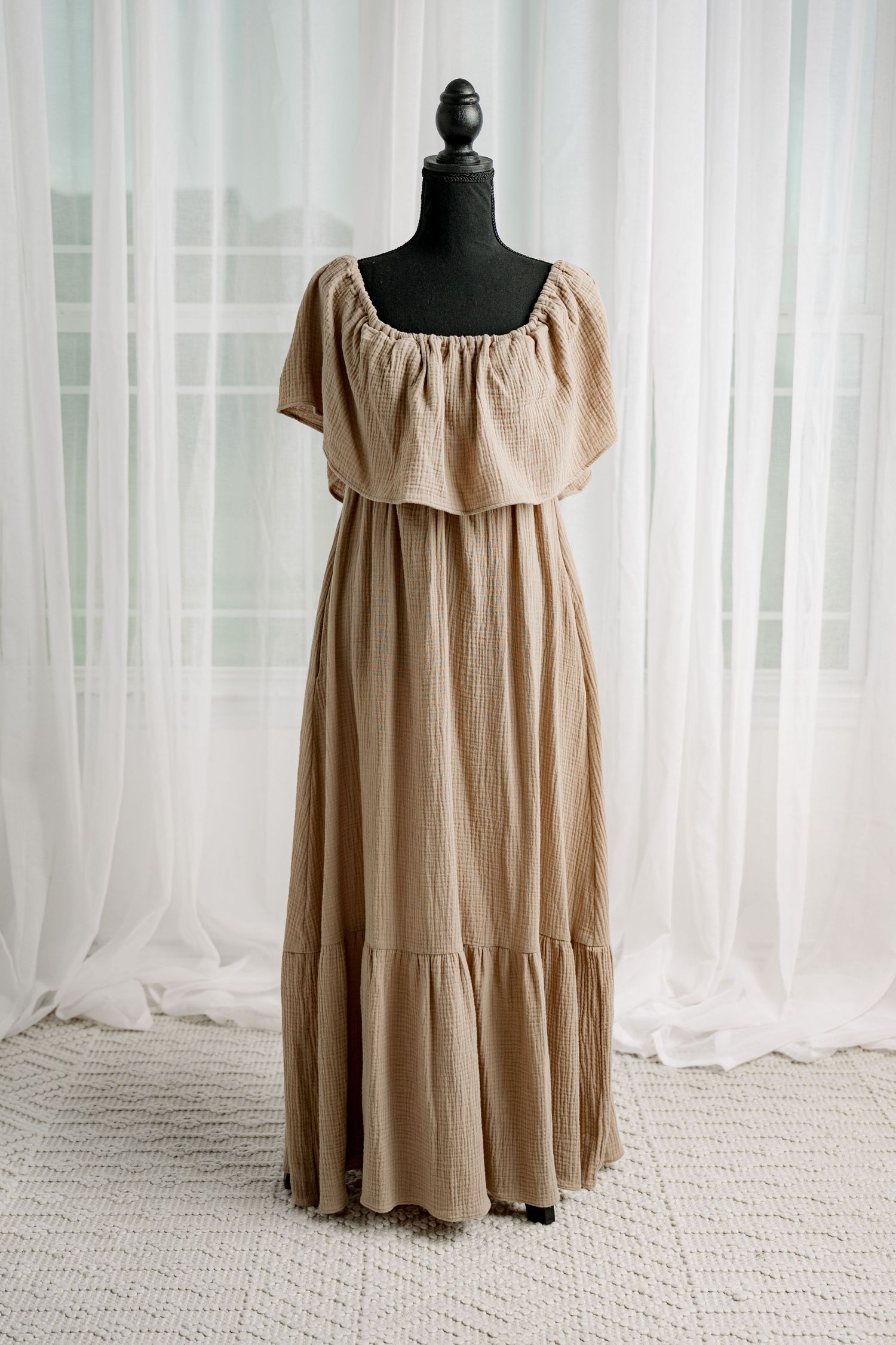 Beige off-shoulder tiered maxi dress with ruffled neckline on mannequin.