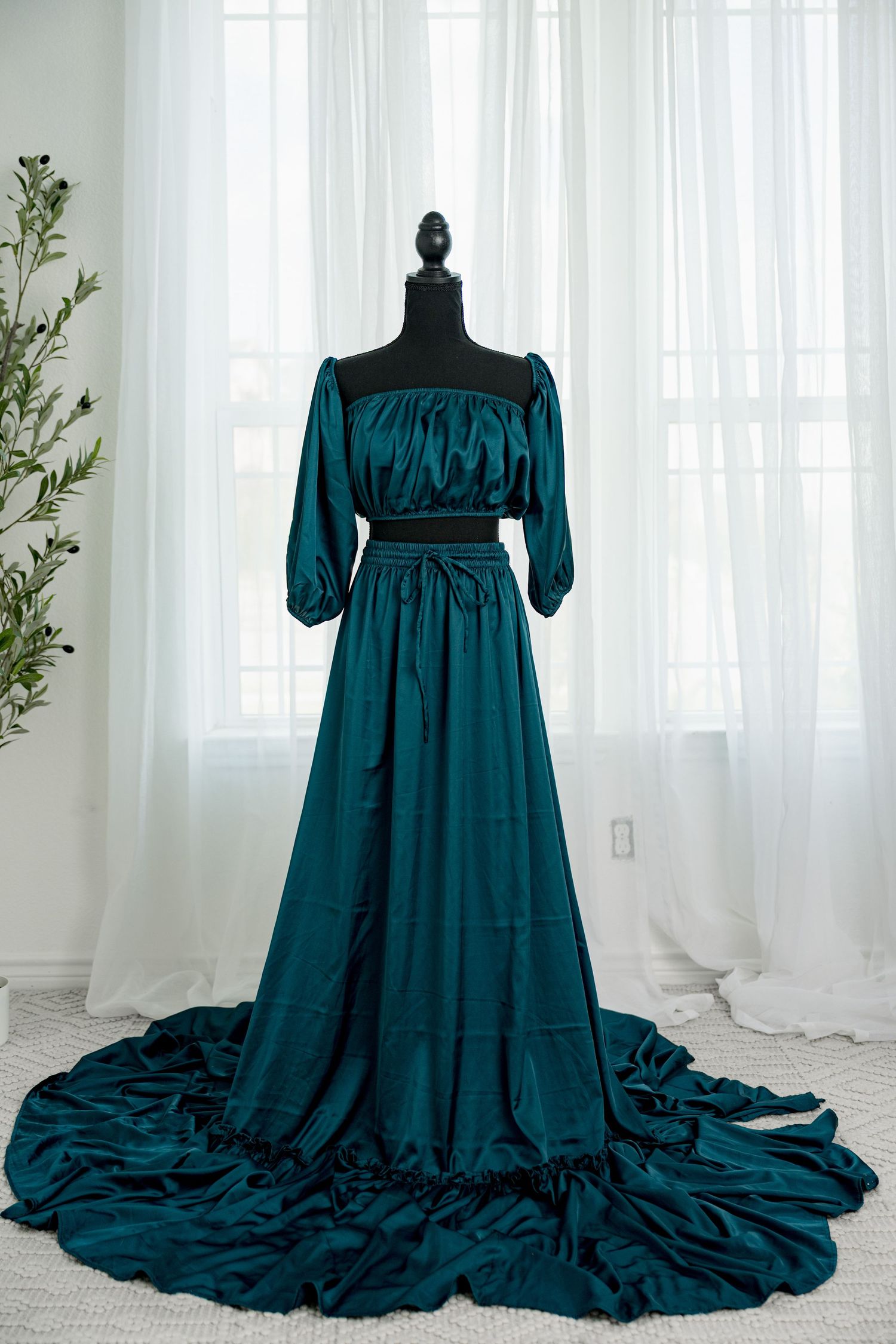 Teal satin off-shoulder long sleeve tiered maxi dress with train displayed on a black mannequin.