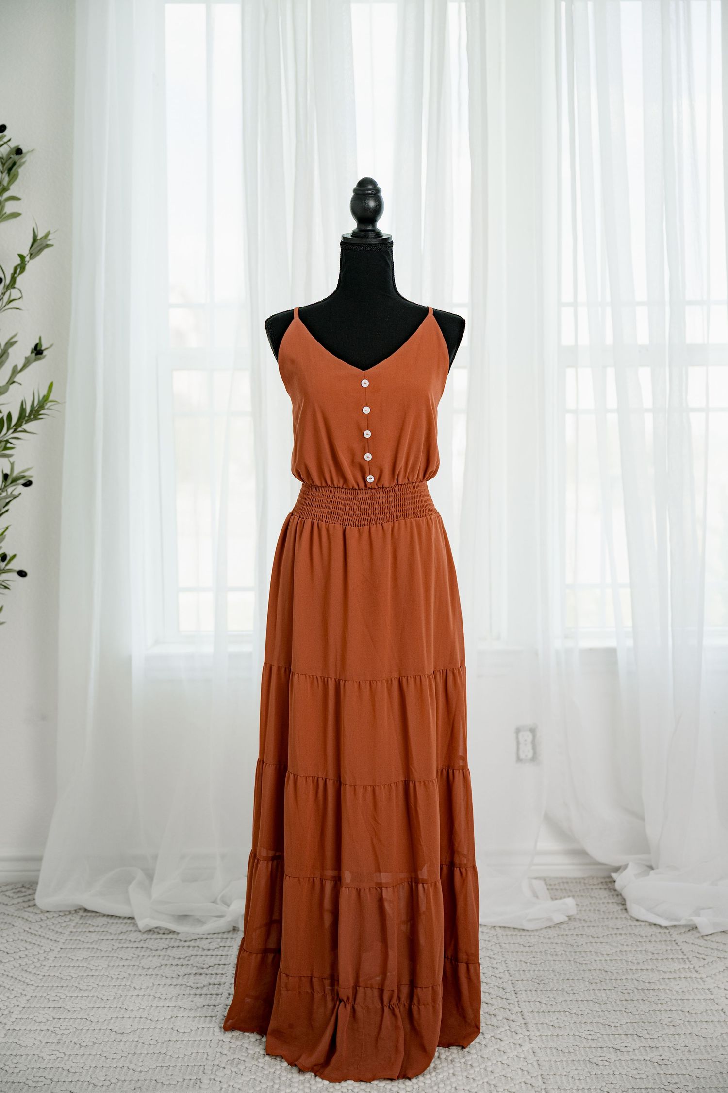 Rust orange spaghetti strap tiered maxi dress with button detail on a black mannequin.