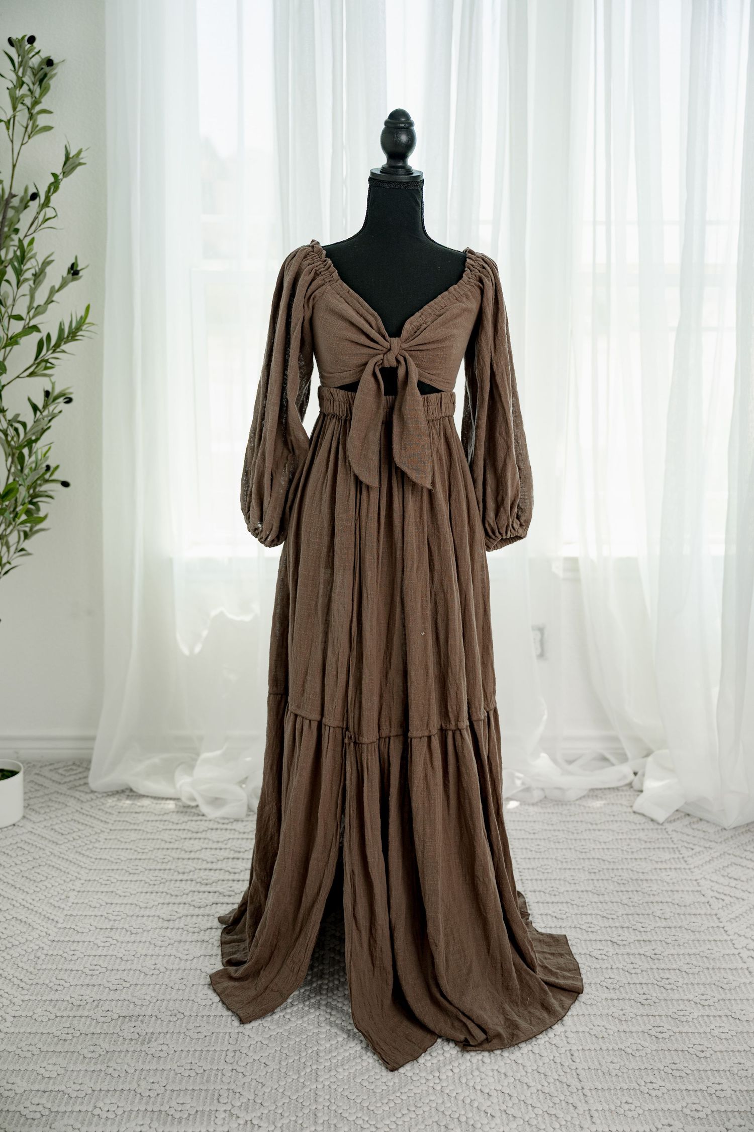 Brown boho maxi dress with long puff sleeves, front tie detail, and tiered skirt with train on mannequin.