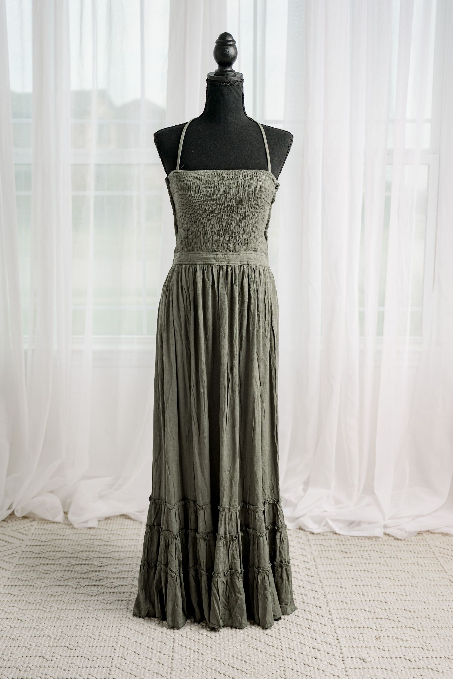 Olive green smocked bodice spaghetti strap maxi dress with ruffle hem on mannequin.