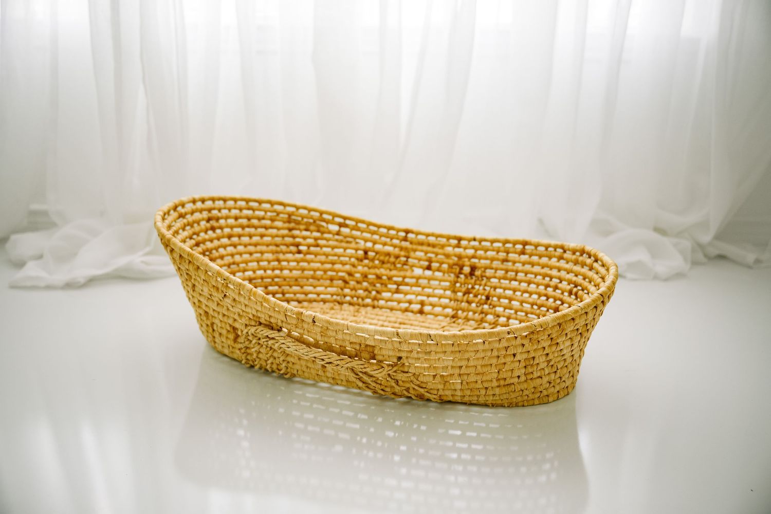 Oval woven golden straw basket on a white reflective floor.