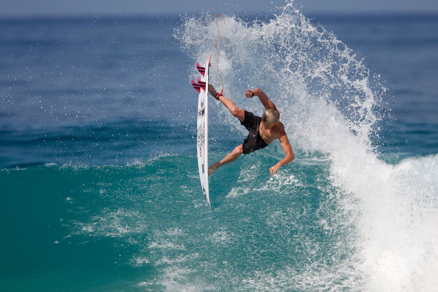 A surfer performs an aerial maneuver with their surfboard above turquoise ocean waves during a dynamic ride.