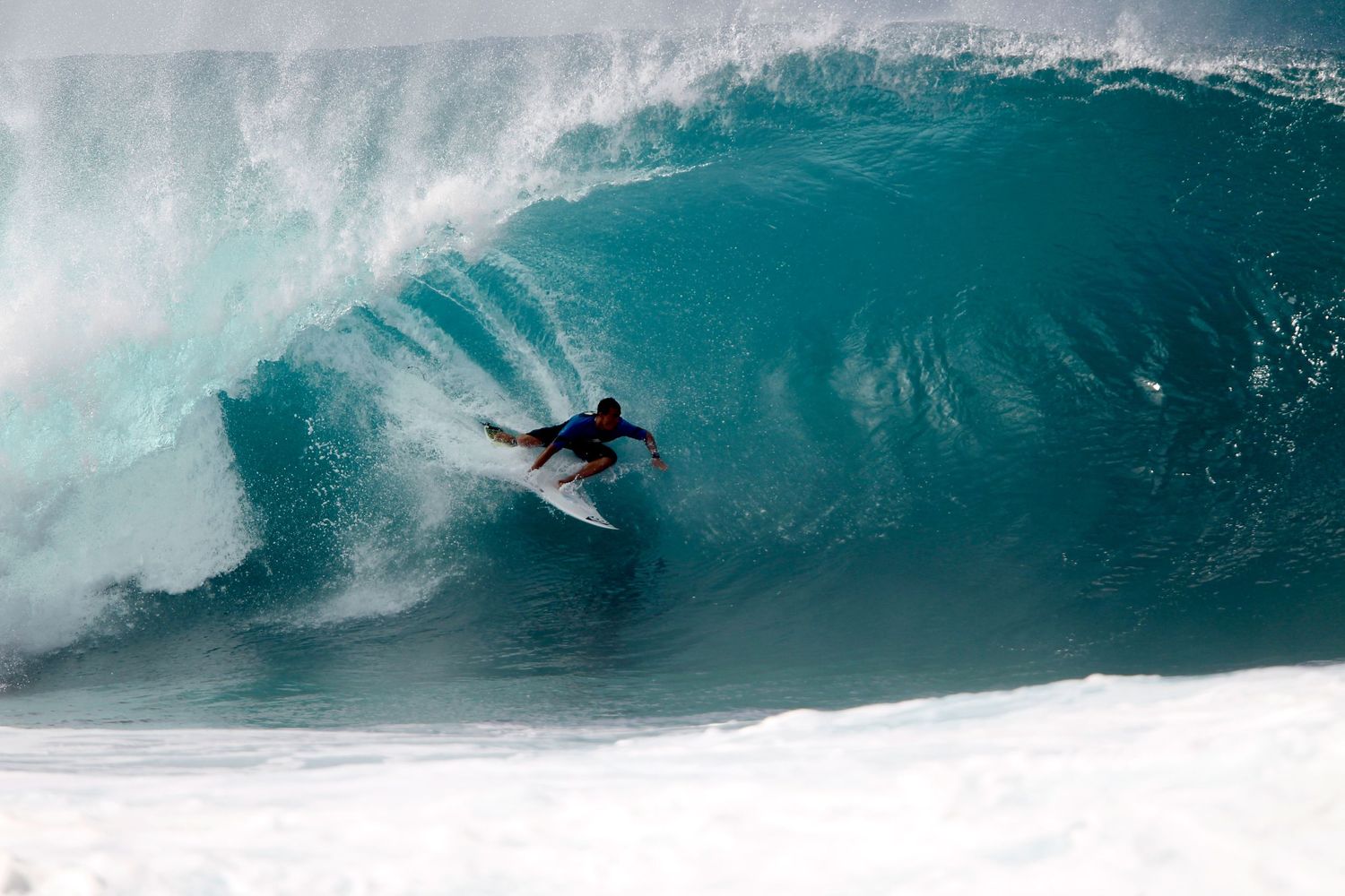 A surfer rides inside a massive turquoise wave barrel at a tropical surf break.