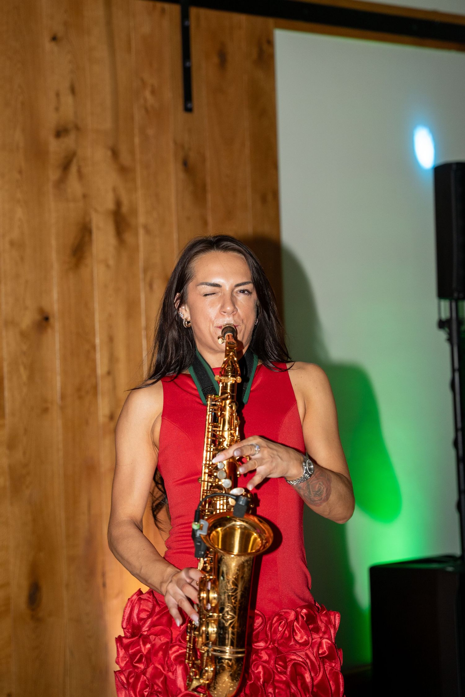 Woman in red dress passionately playing a gold saxophone on stage with green and blue stage lighting.