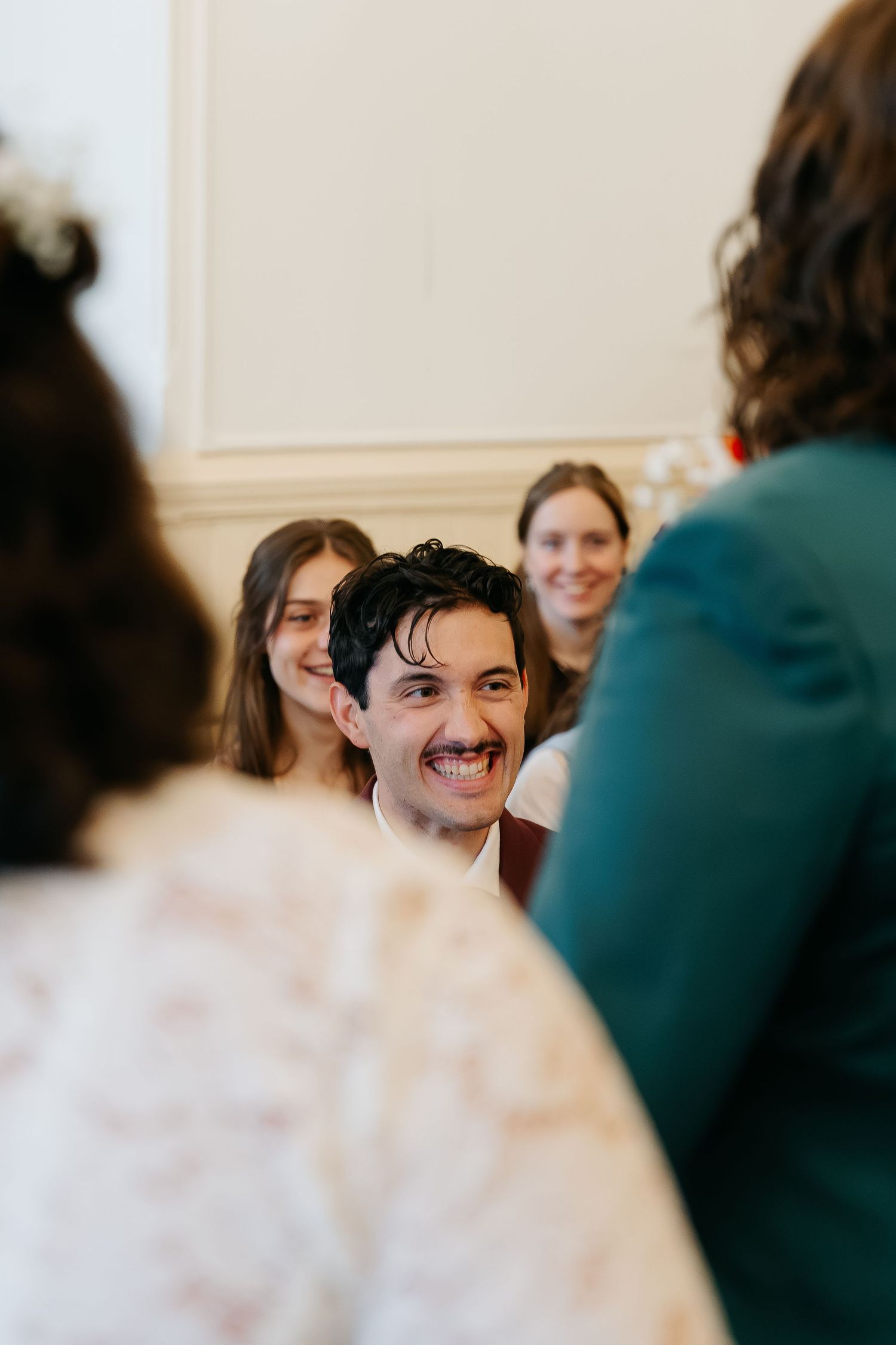 Smiling groom at wedding ceremony surrounded by guests in elegant white venue.