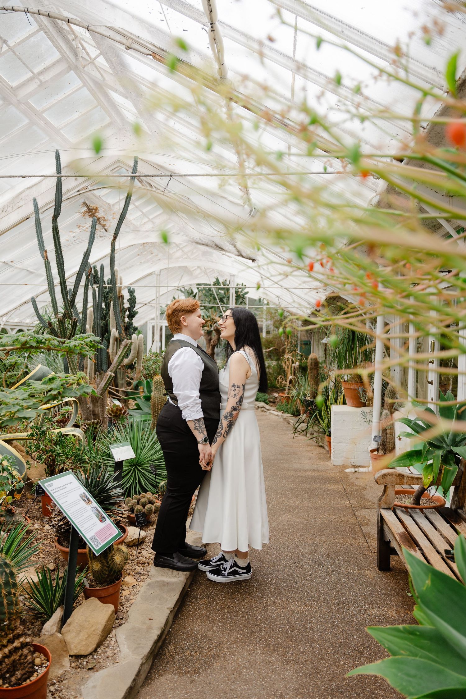 Couple holding hands in a lush greenhouse wedding portrait surrounded by cacti and tropical plants.