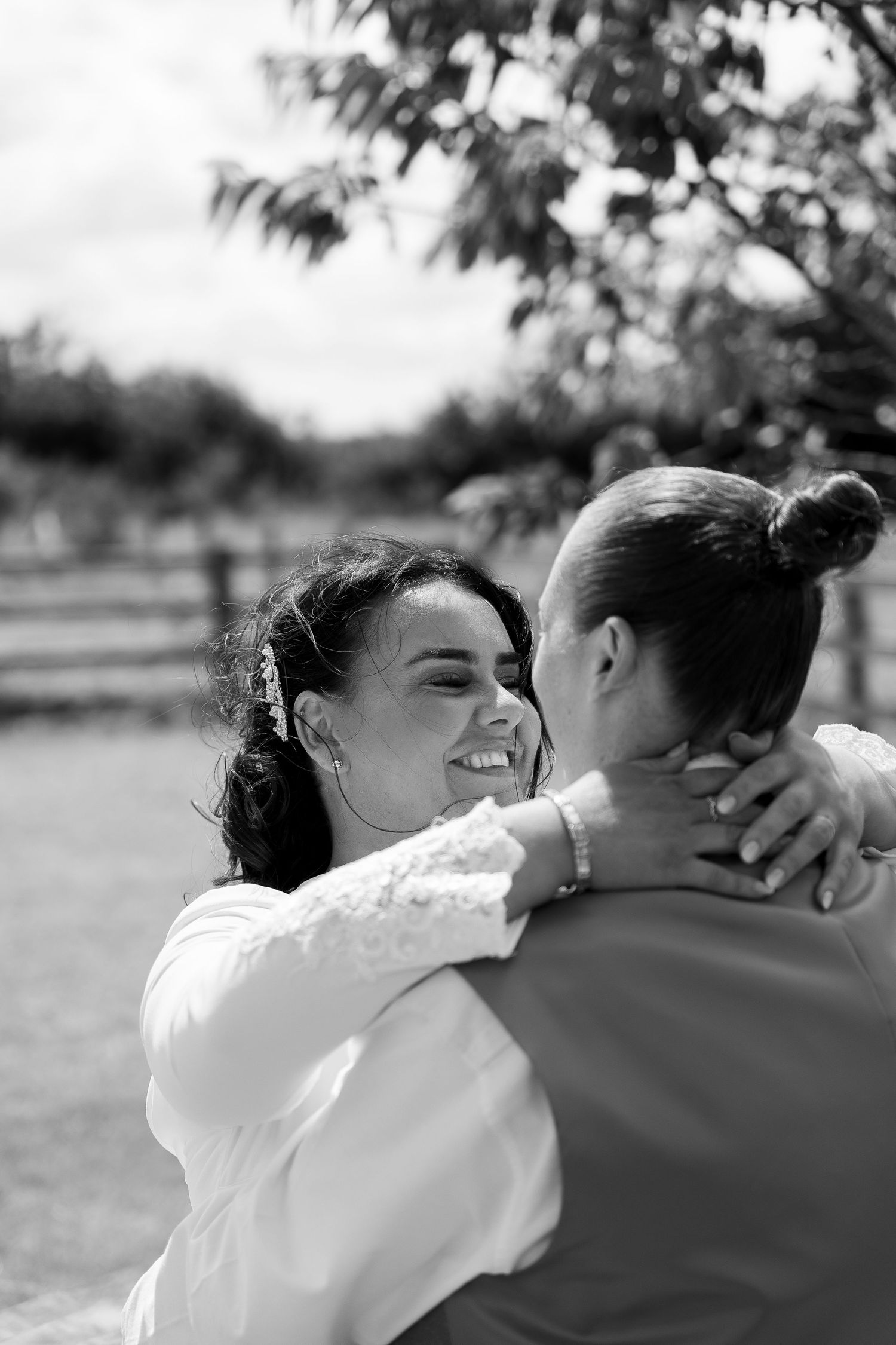 Black and white photo of a smiling bride embracing her partner outdoors on their wedding day.