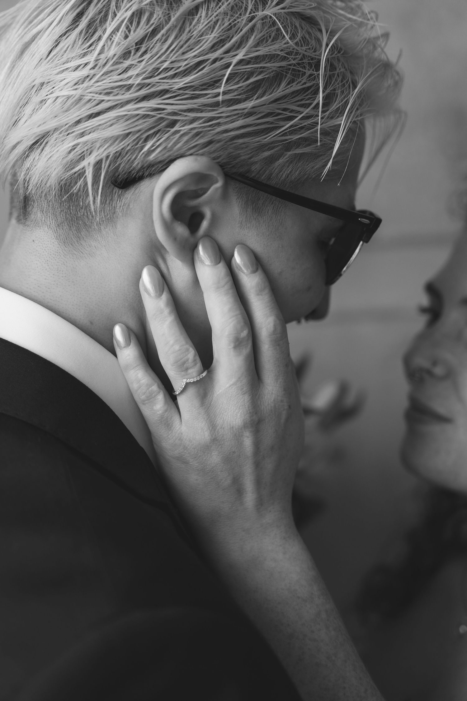 Black and white photo of a woman with short blonde hair and glasses, with a hand gently touching her face.