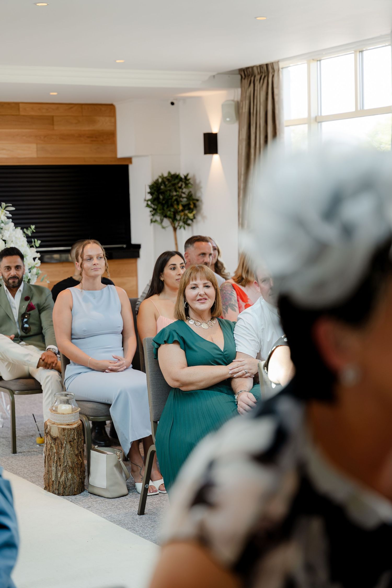 Wedding guests seated indoors, watching a ceremony in an elegant venue with greenery decor.