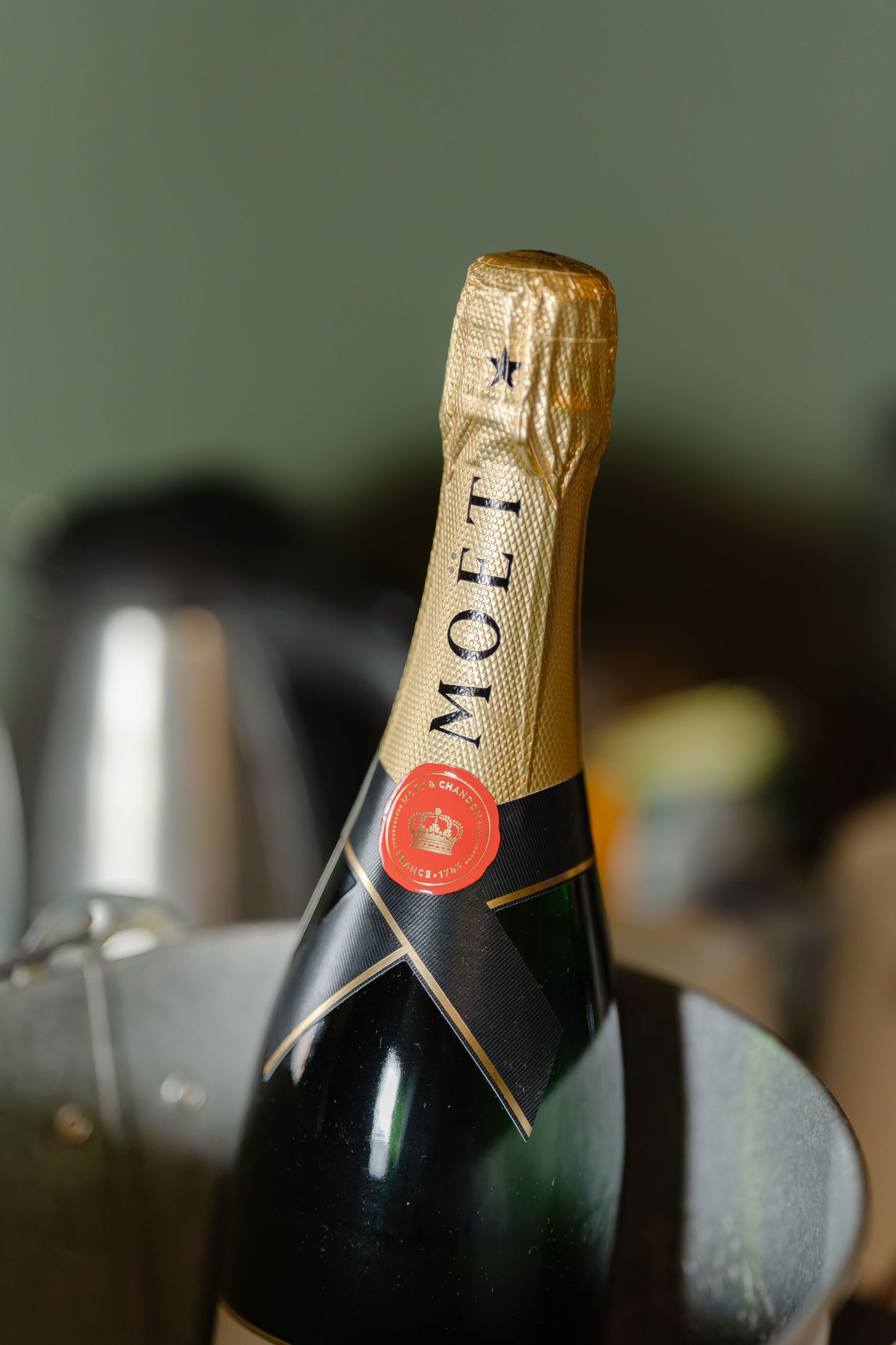 Close-up of a Moet & Chandon champagne bottle with gold foil neck and red wax seal, set against a soft green background.