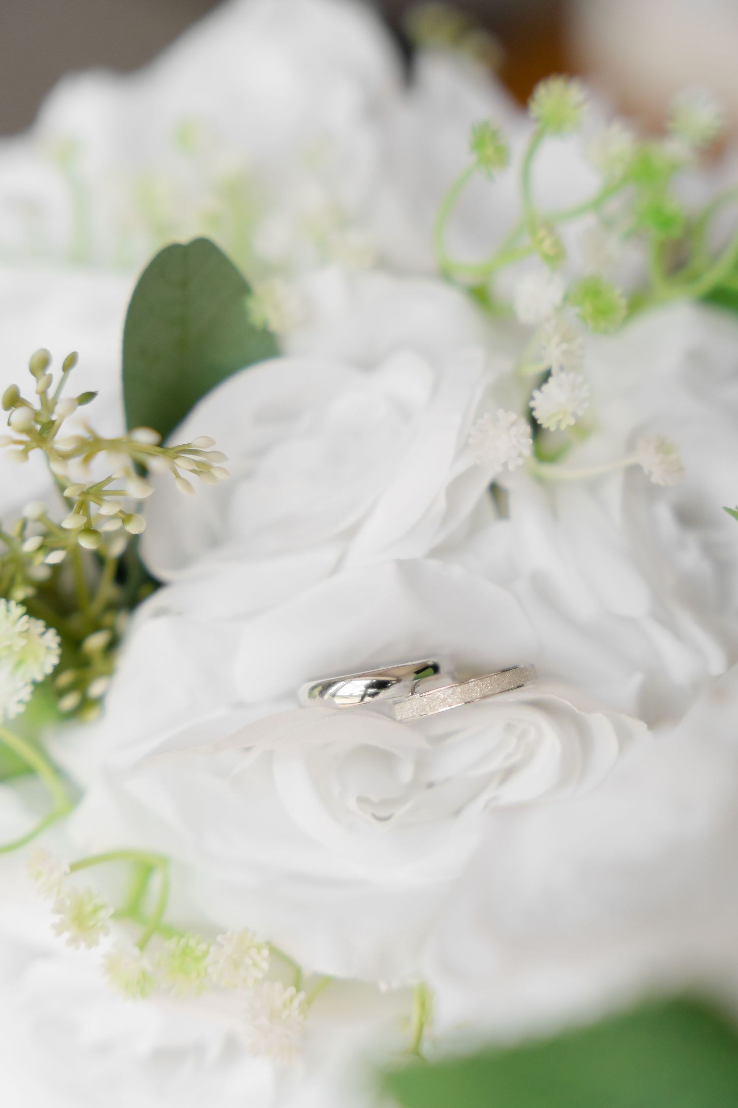 Two silver wedding rings resting on white roses in a bridal bouquet with green accents.