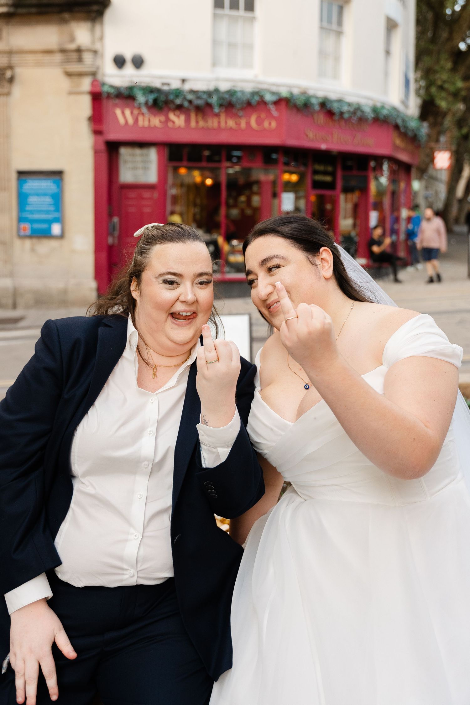 Two brides laughing and showing off wedding rings outside Wine St Barber Co in Bristol.