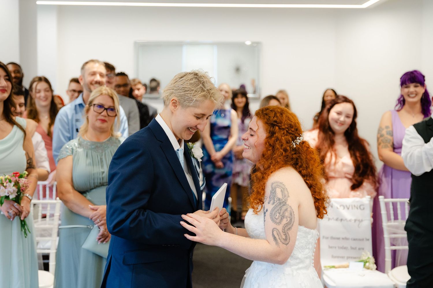 Bride and groom share a joyful moment during wedding ceremony, surrounded by smiling guests in a bright modern venue.