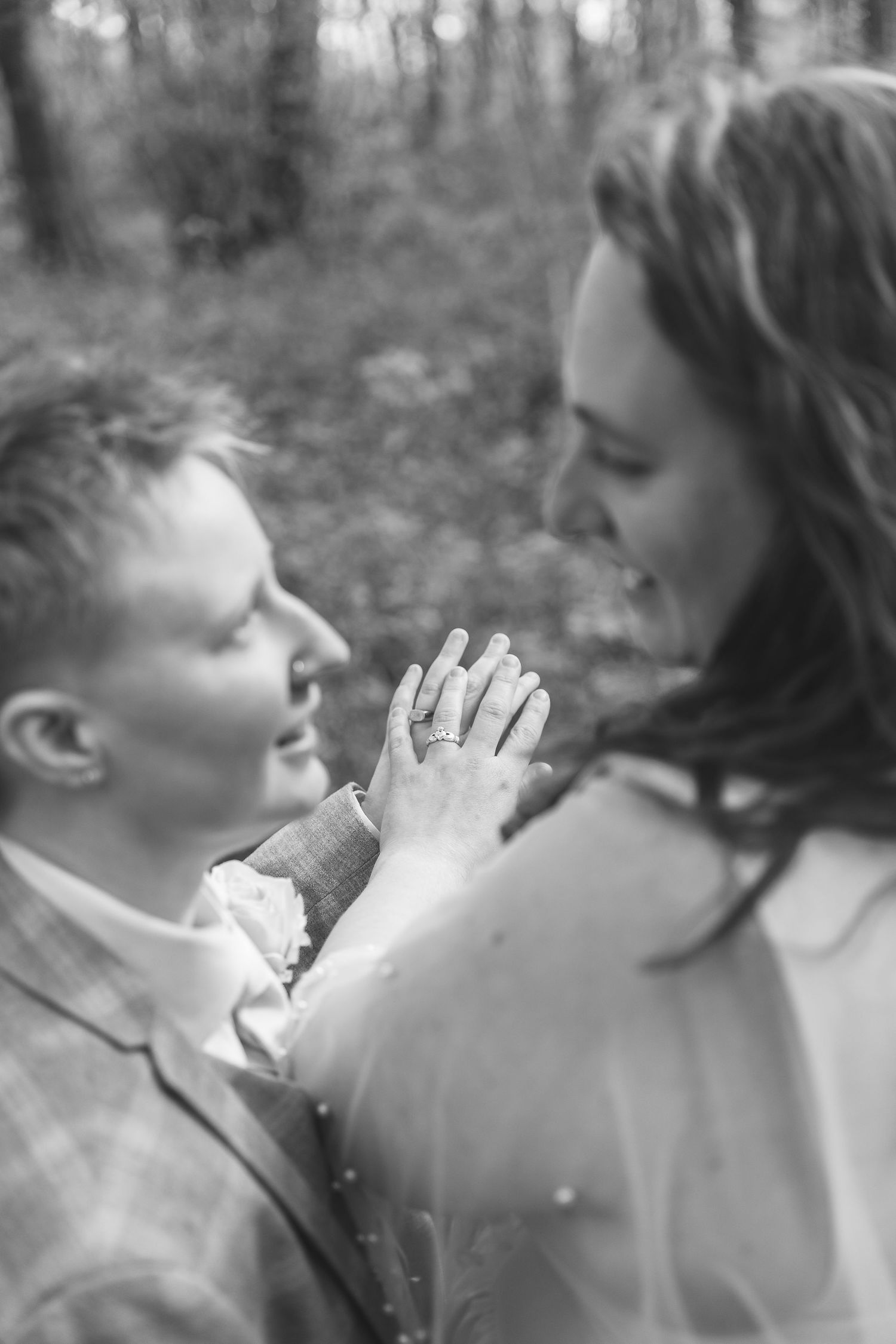 Black and white photo of a couple holding hands showing an engagement ring in a forest setting.