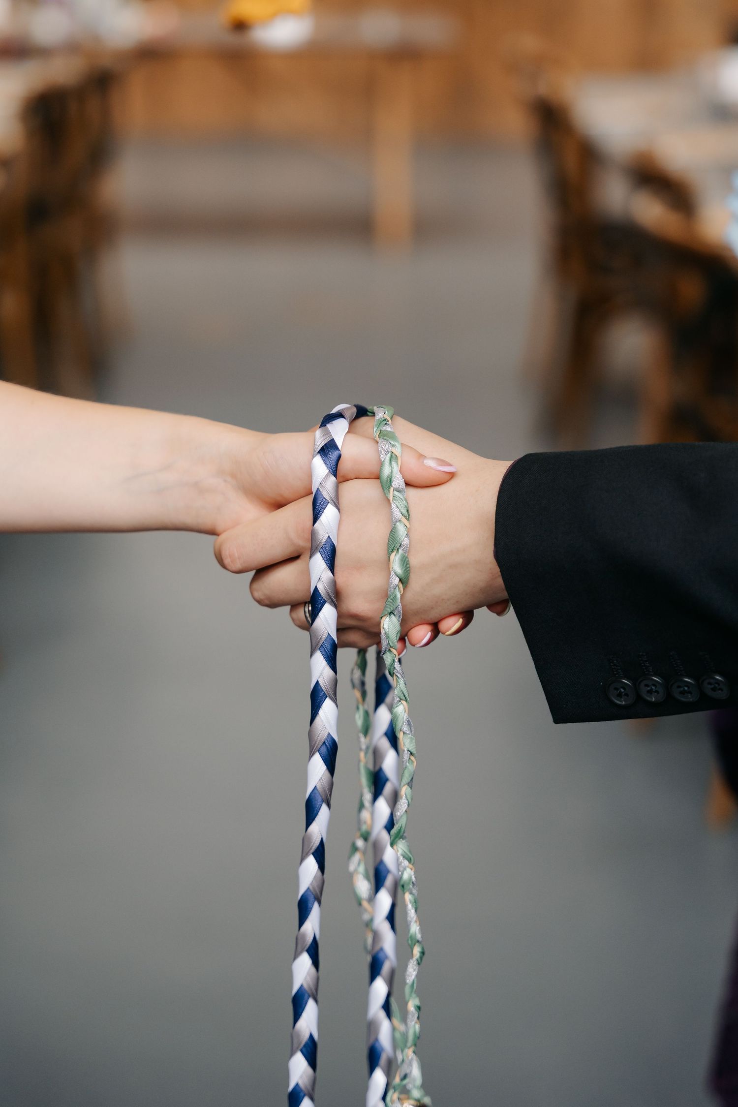 Two hands clasped together bound by braided blue, white, and green cords during a handfasting wedding ceremony.