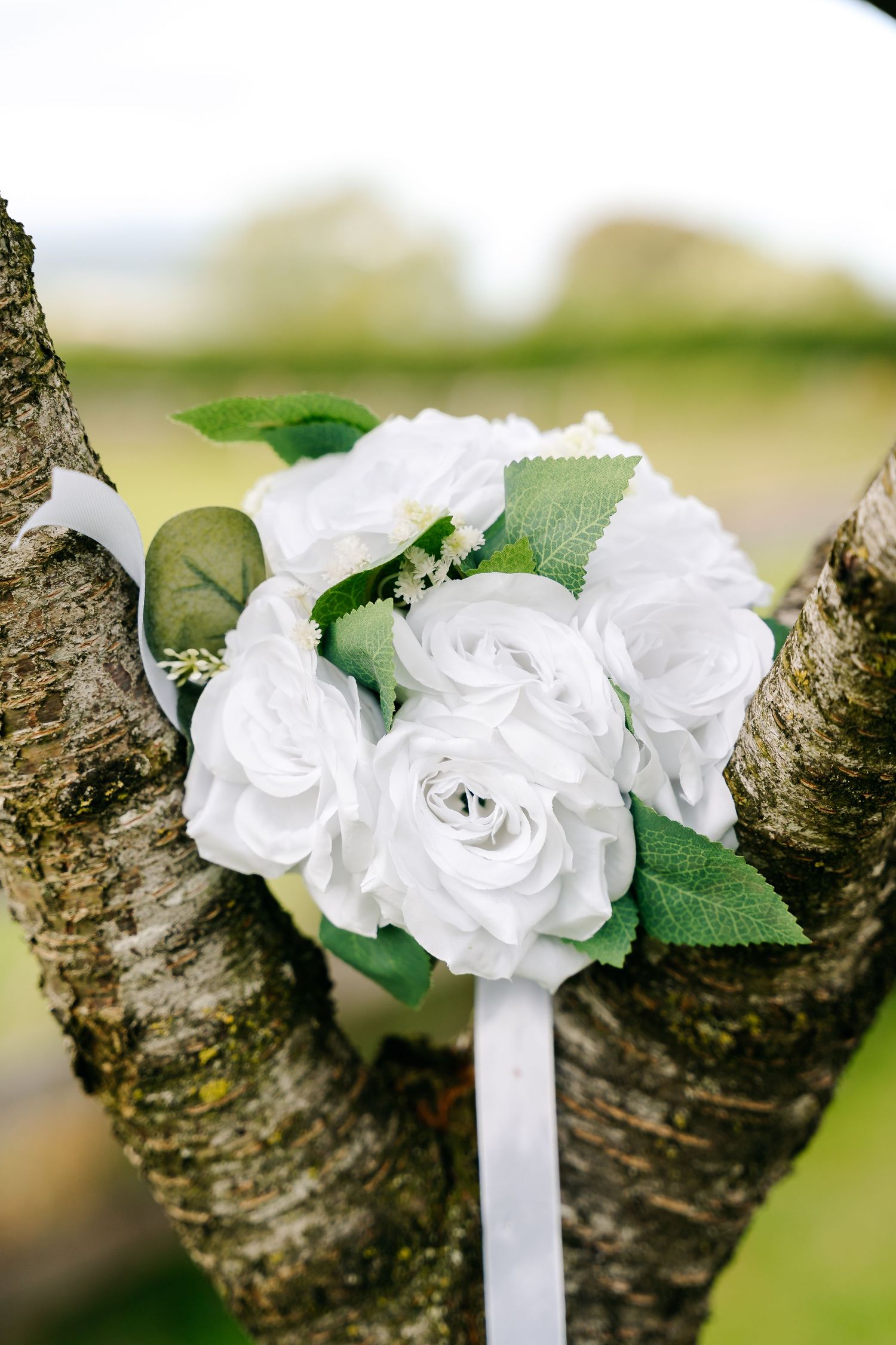 White rose bouquet with green leaves resting in tree branches, perfect for a wedding or special occasion.