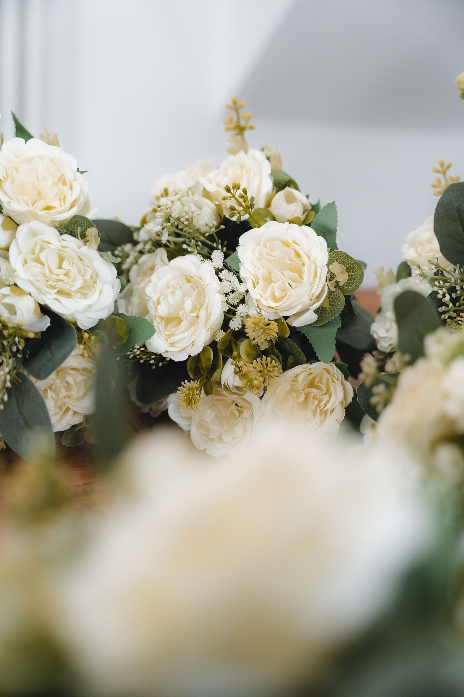 Elegant wedding floral arrangement featuring white garden roses, eucalyptus, and gold accent flowers in a soft, romantic display.