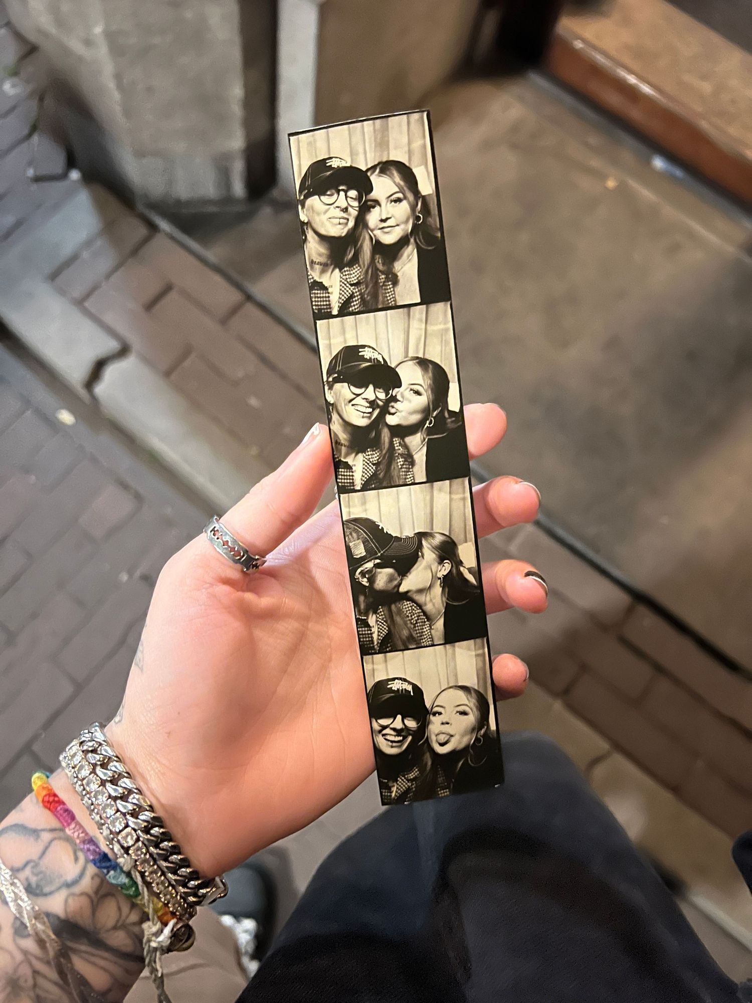 Hand holding a black and white photo booth strip showing two people posing together in three fun snapshots.