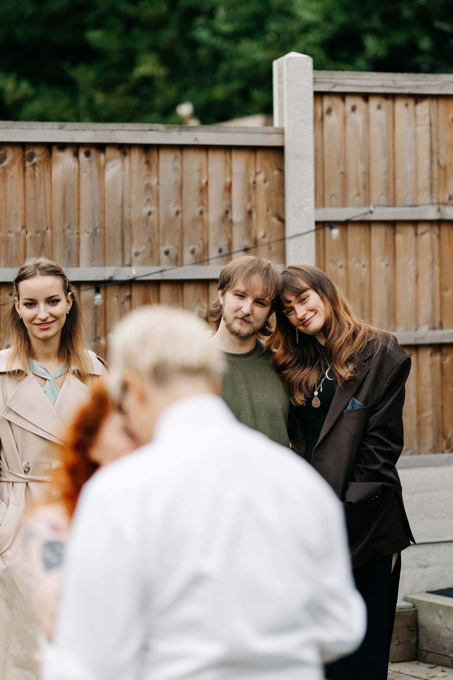 Group of friends smiling outdoors near wooden fence at casual backyard gathering.