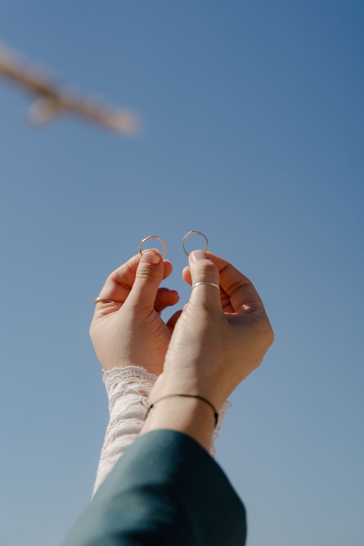 Two hands holding gold wedding rings up against a clear blue sky on a sunny day.