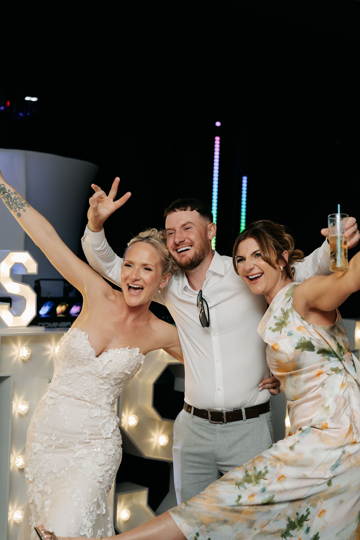Bride in white lace gown celebrates with guests at outdoor wedding reception at night.