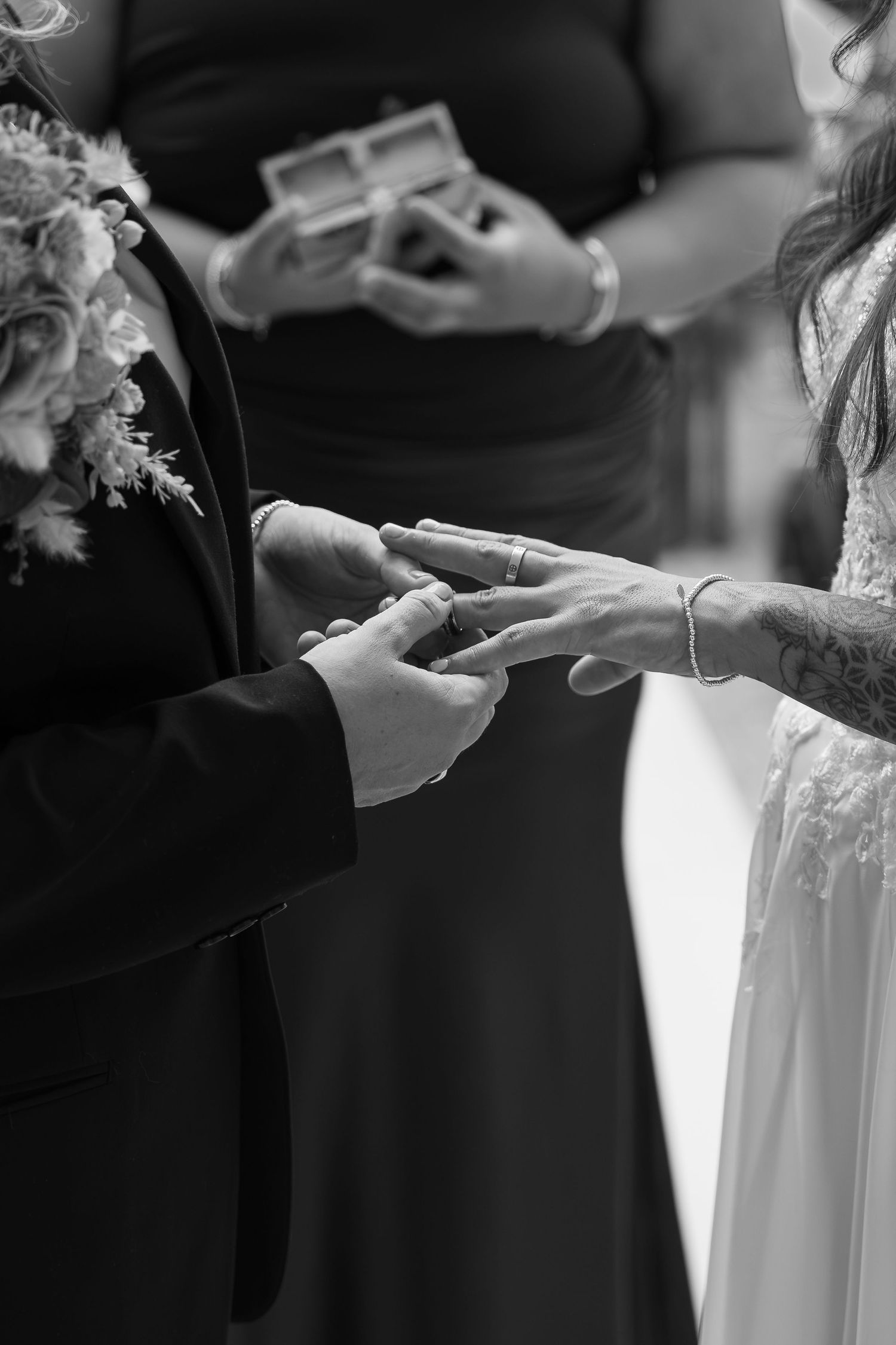 Black and white photo of bride and groom exchanging wedding rings during ceremony.