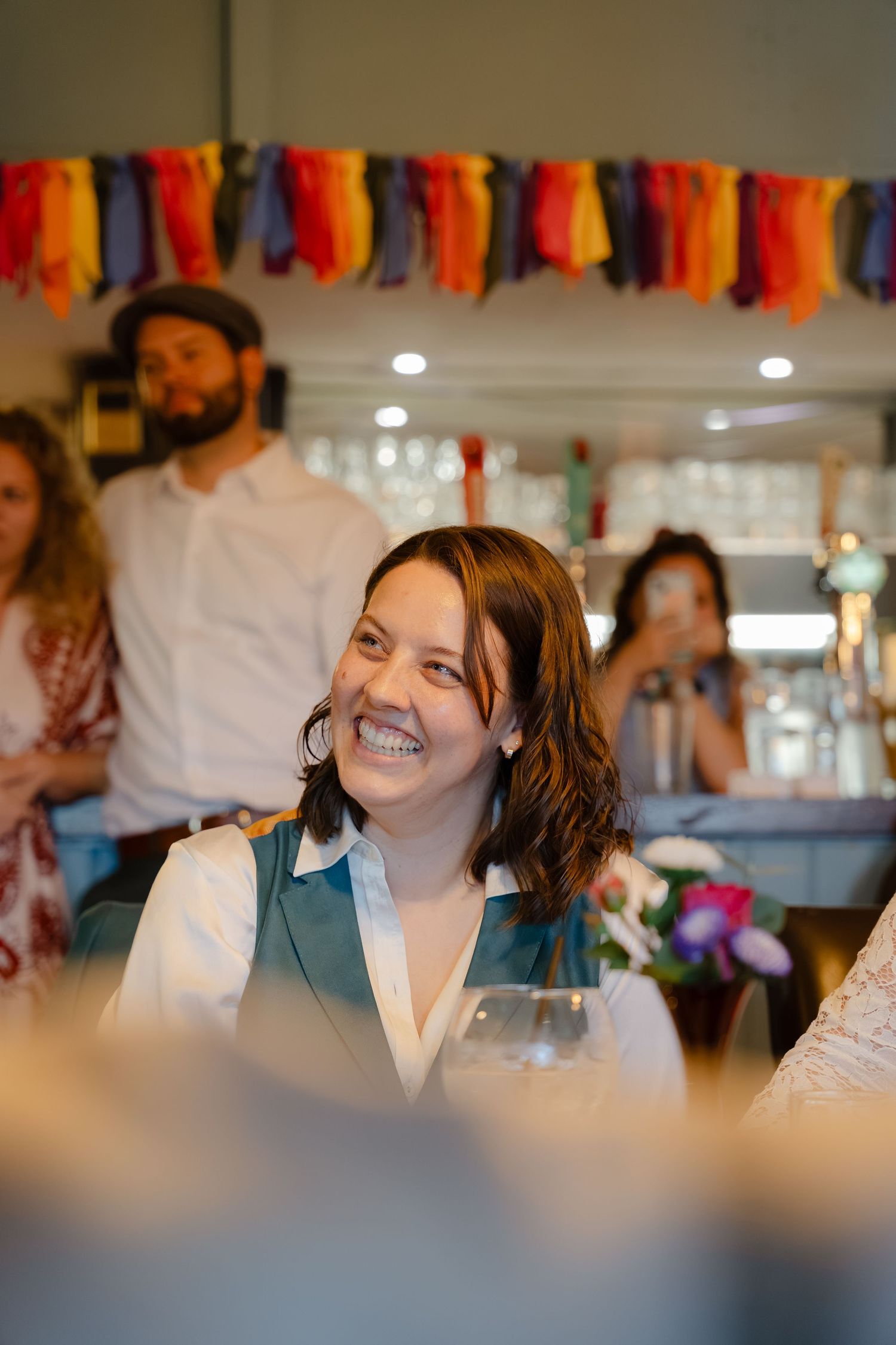 Smiling woman holding wine glass at festive indoor gathering with colorful tassel decorations.