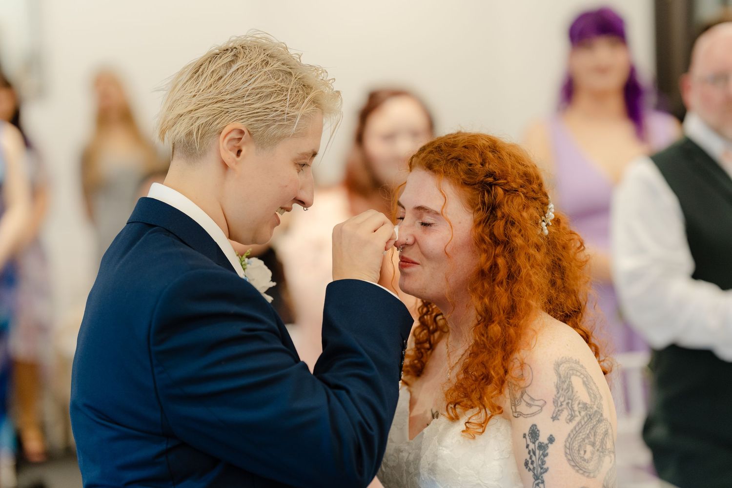 Two brides share a tender moment during their wedding ceremony, one in a blue suit and one in a white gown.